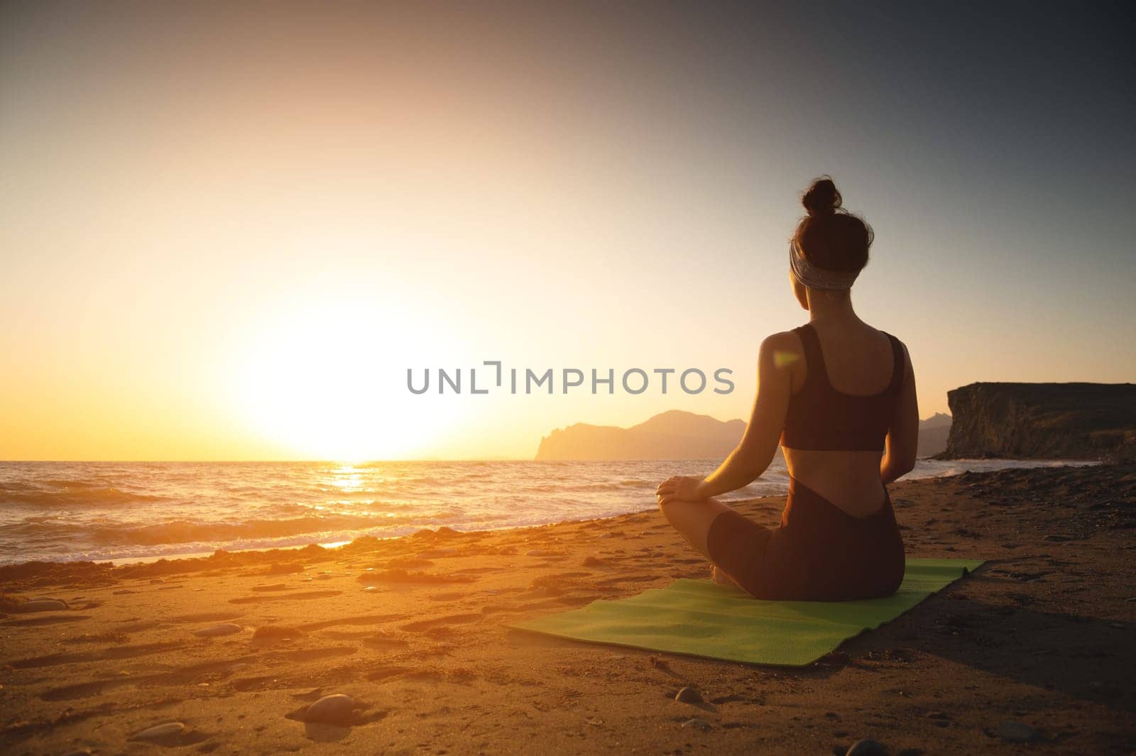 Yoga woman meditating at serene sunset or sunrise on the beach. The girl relaxes in the lotus position. Fingers folded in mudras