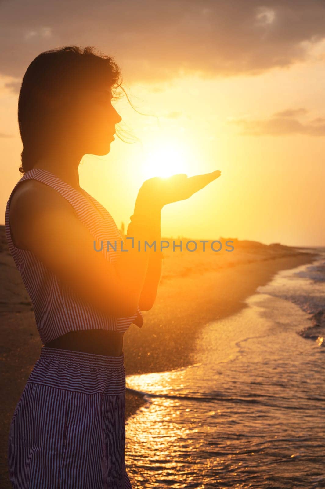 Silhouette of a young Caucasian woman holding the sun in her hands. On the seashore at sunset. by yanik88