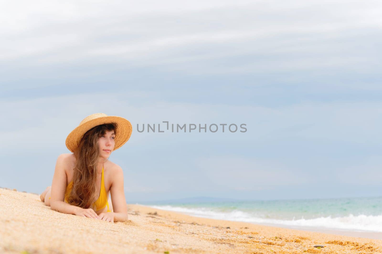 Summer vacation. A woman in a bikini and sun hat enjoys tanning on the beach. A model in a swimsuit sunbathes against a background of blue sky and tropical sea.