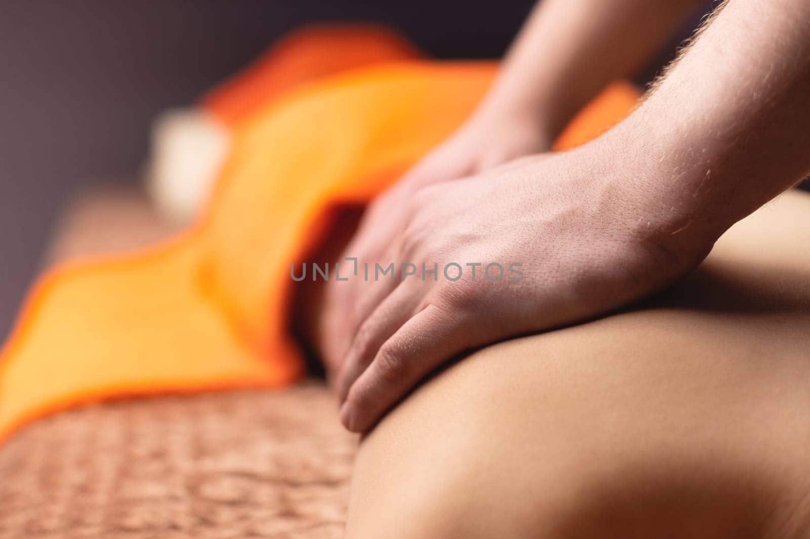Close-up shot of an unrecognizable male masseur making massage movements on the back of a young woman, preventing spinal pain, lying on a massage table in a spa salon. Body care concept by yanik88