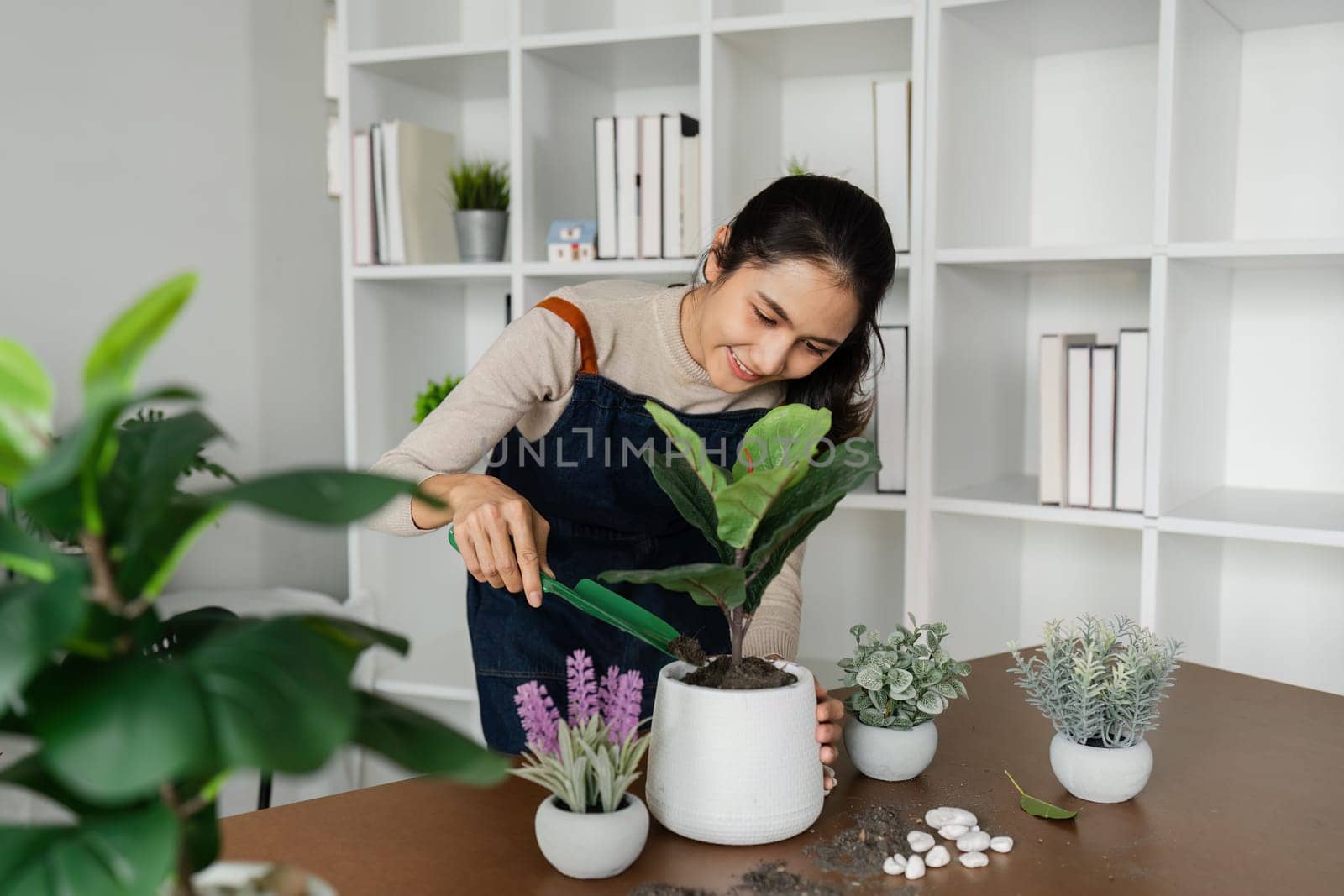 A woman is planting a plant in a white pot. The plant is surrounded by other plants in different pots