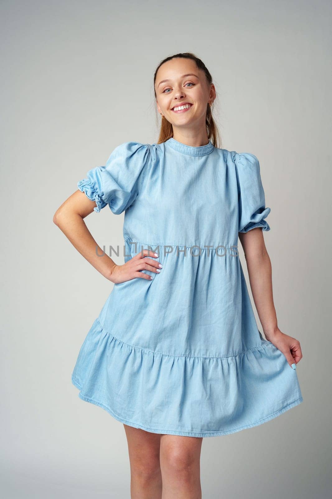 Young happy smiling woman in a light blue dress on a gray background close up