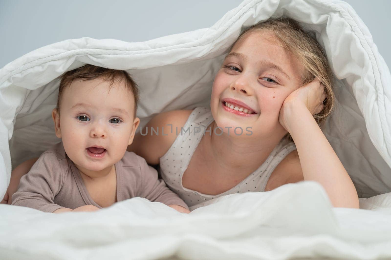 Little girl and her newborn brother hiding under the blanket