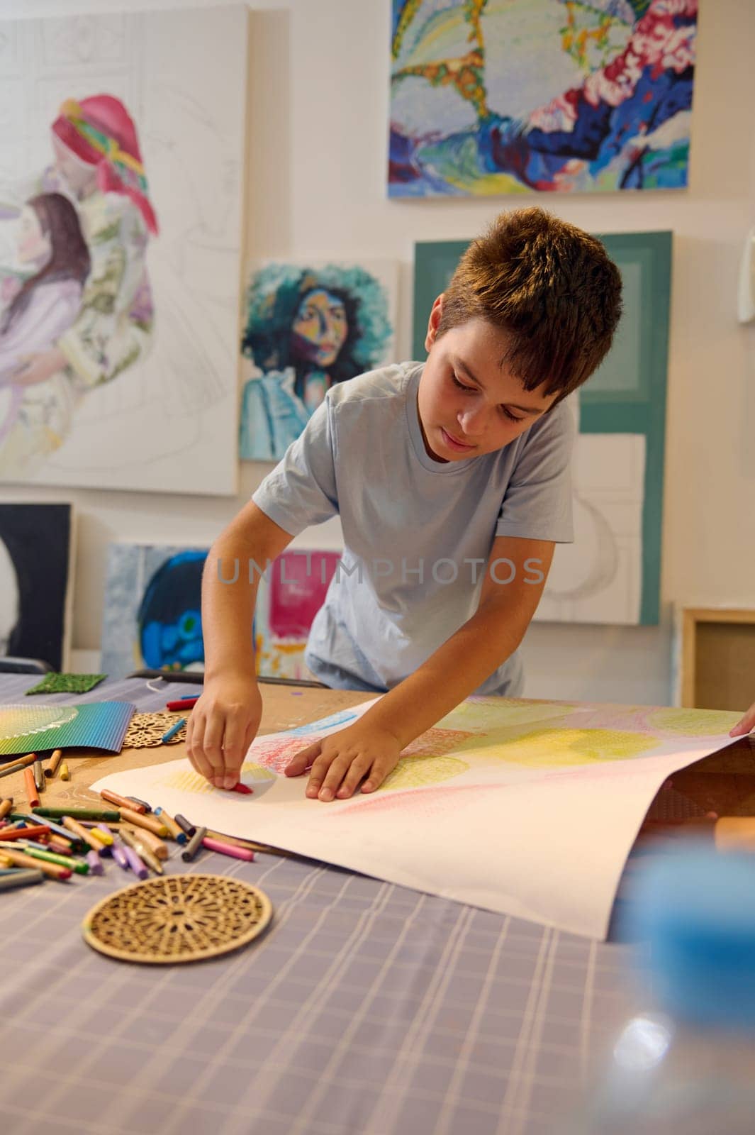Teenage schoolboy drawing with pastel pencils on a white paper sheet