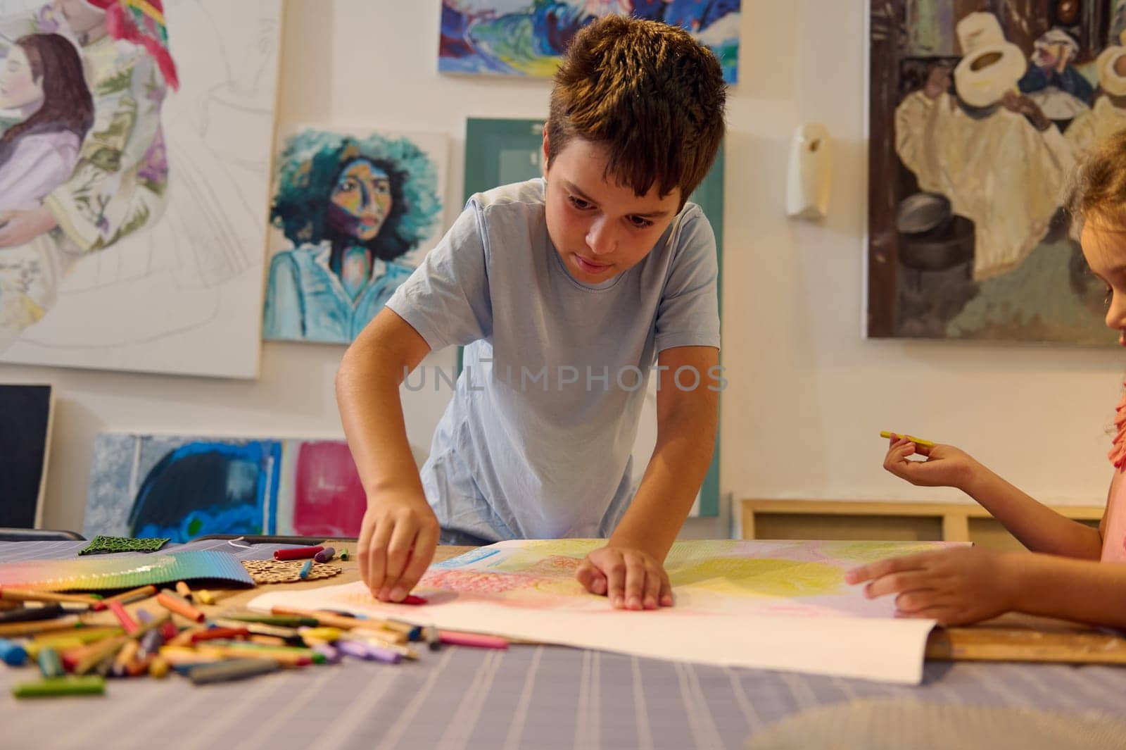Teenage schoolboy taking pencil from the pile of colorful pencils, drawing picture in the creative art school by artgf