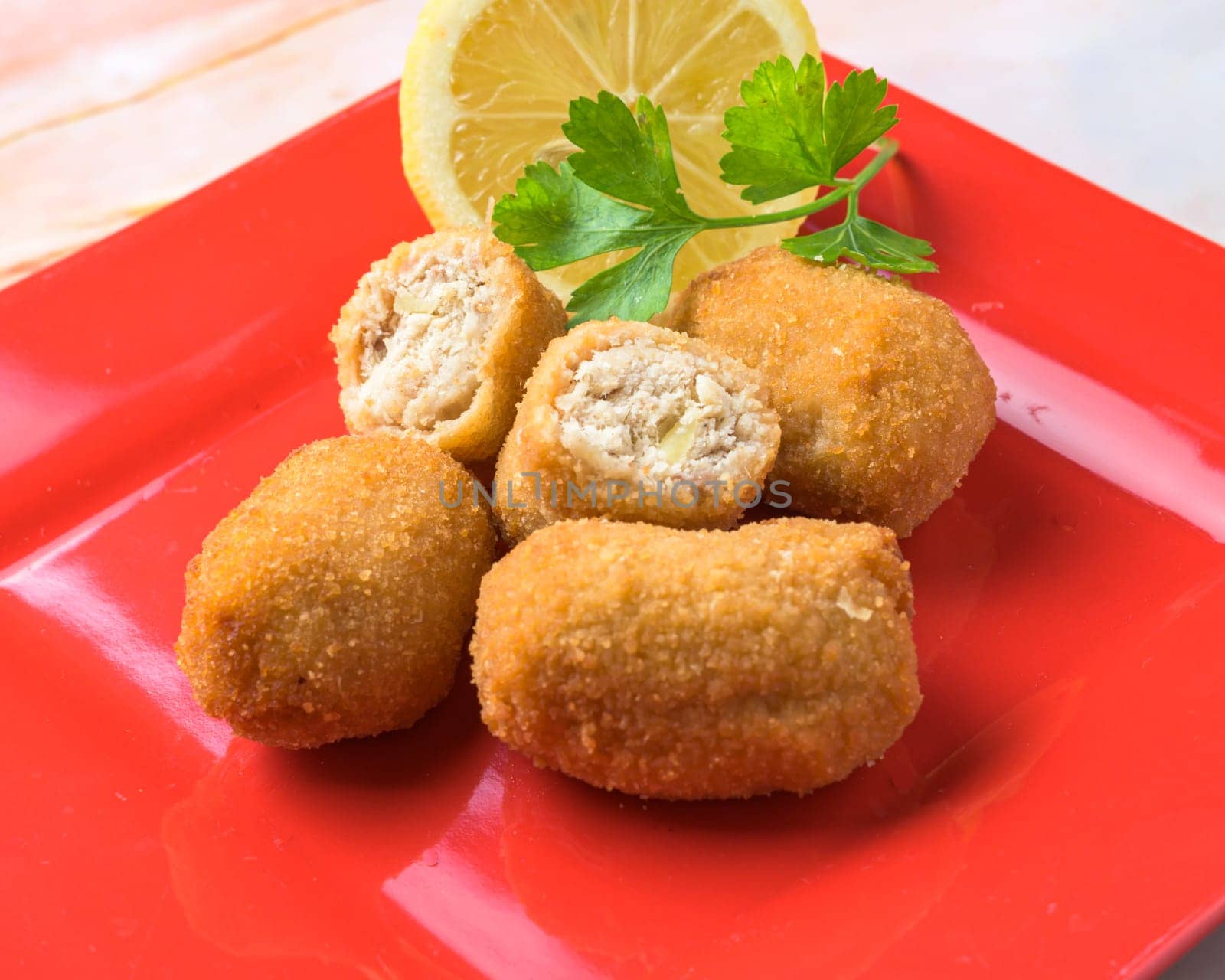 Fried croquettes served with a lemon wedge and parsley on a red plate, typical food, typical mediterranean mallorcan cuisine typical from balearic islands mallorca, spain by carlosviv