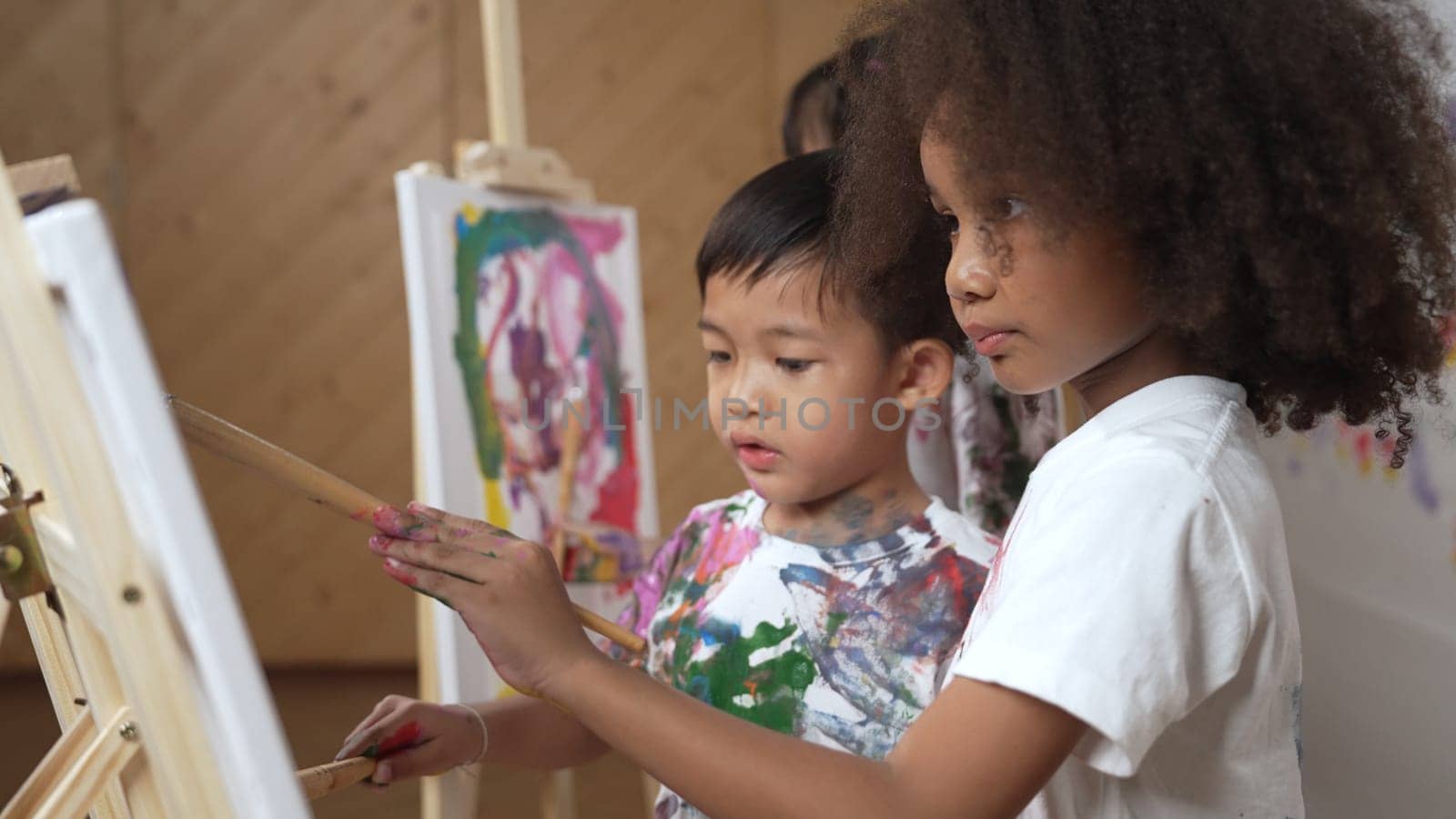 Creative african girl painted or draw canvas together with asian boy. Erudition. by biancoblue