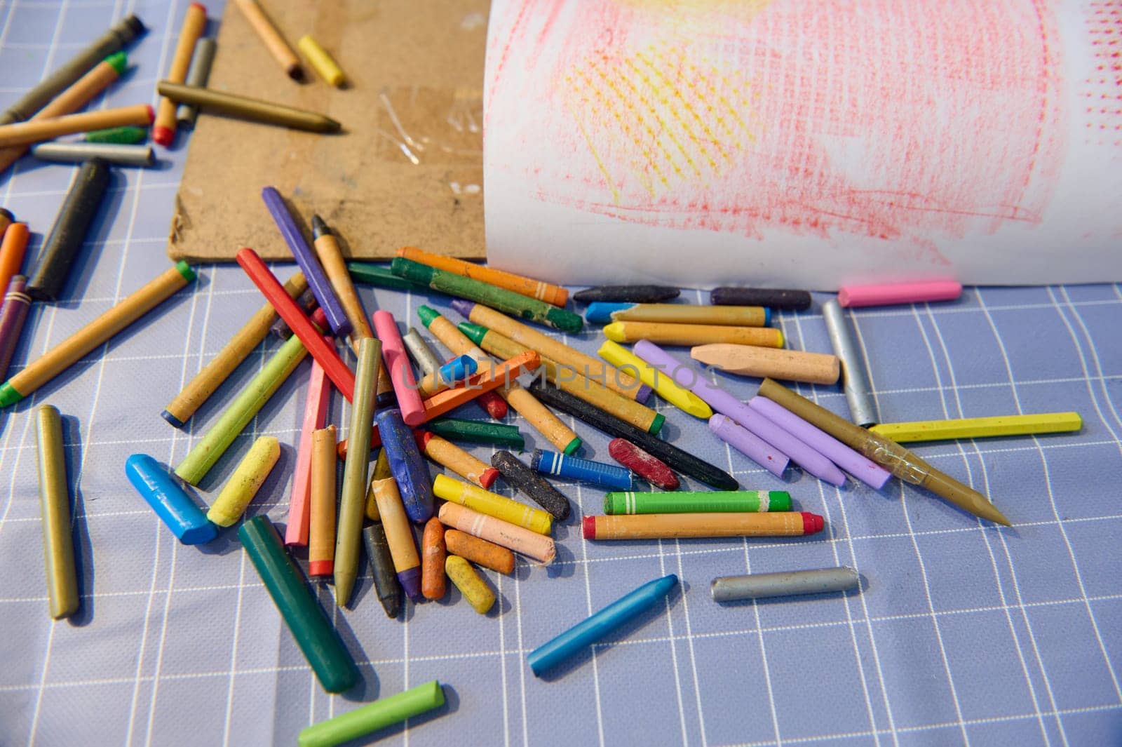 A background with scattered pastel color pencils on a table in the art class. View from above of many colorful crayons lying on the painter's desk. Visual art instruments. Drawing and painting tools