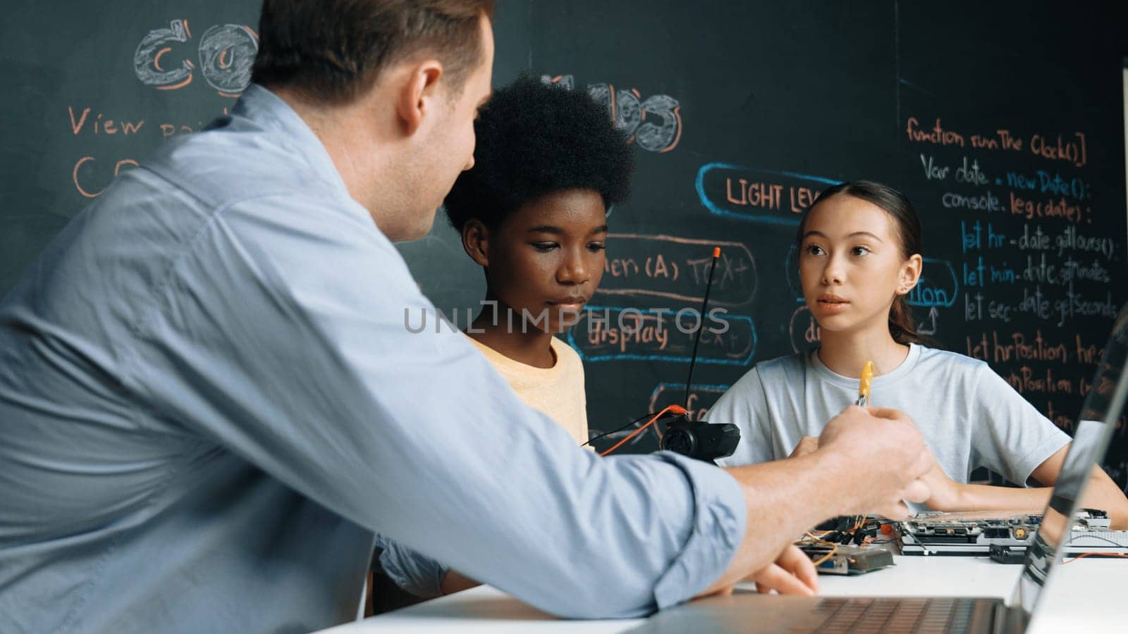 Young cute student fixing controller while teacher pick electronic tool at STEM class. Closeup of professional instructor give advise while smart girl listening carefully and blackboard. Edification.