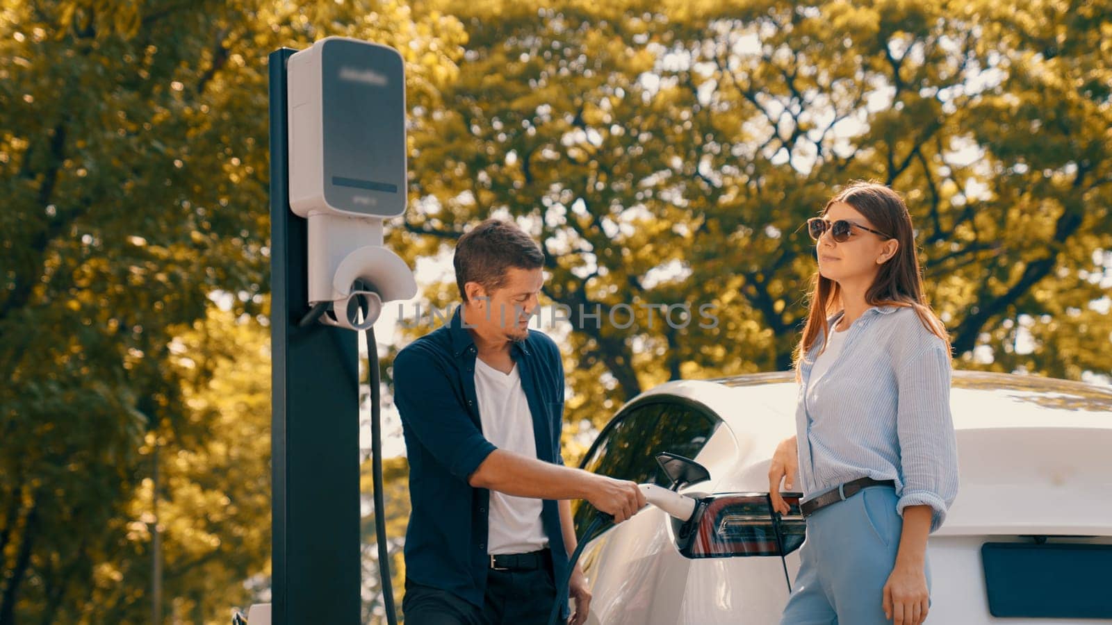 EV car recharging electricity for battery by lovey couple traveling during their road trip travel by eco friendly electric vehicle in national park autumnal forest on holiday. Exalt