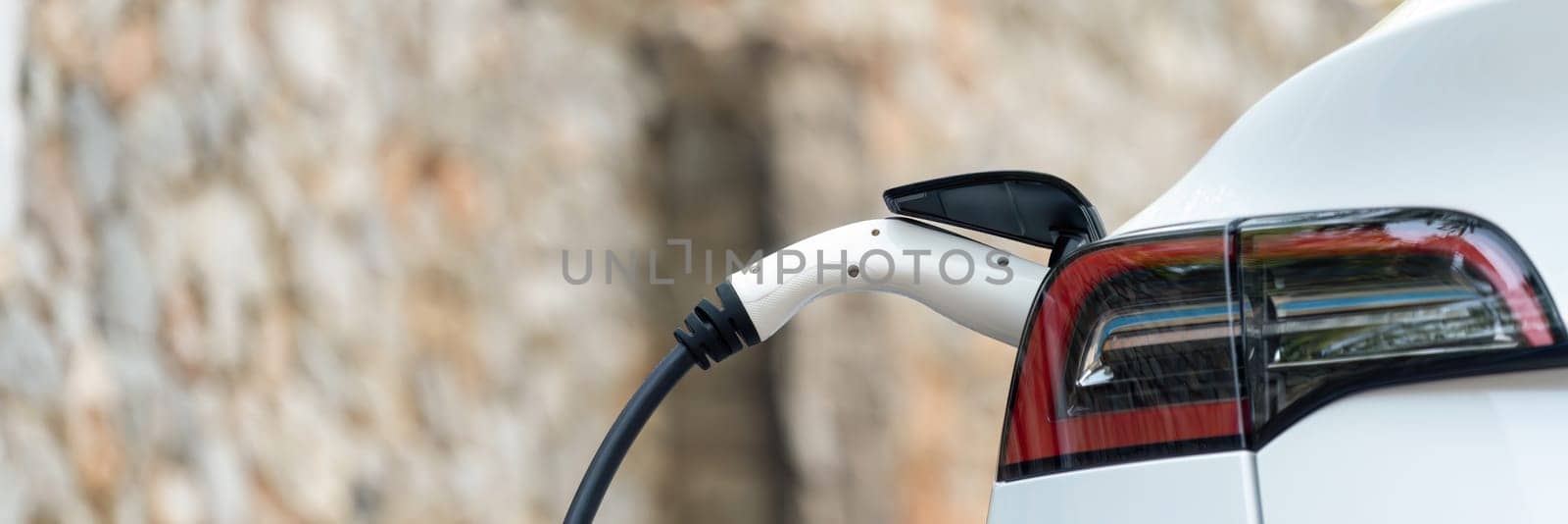 Panorama closeup EV charger handle plugged in or connect to electric car, recharging EV car battery with alternative and sustainable energy with zero CO2 emission for clean environment. Perpetual