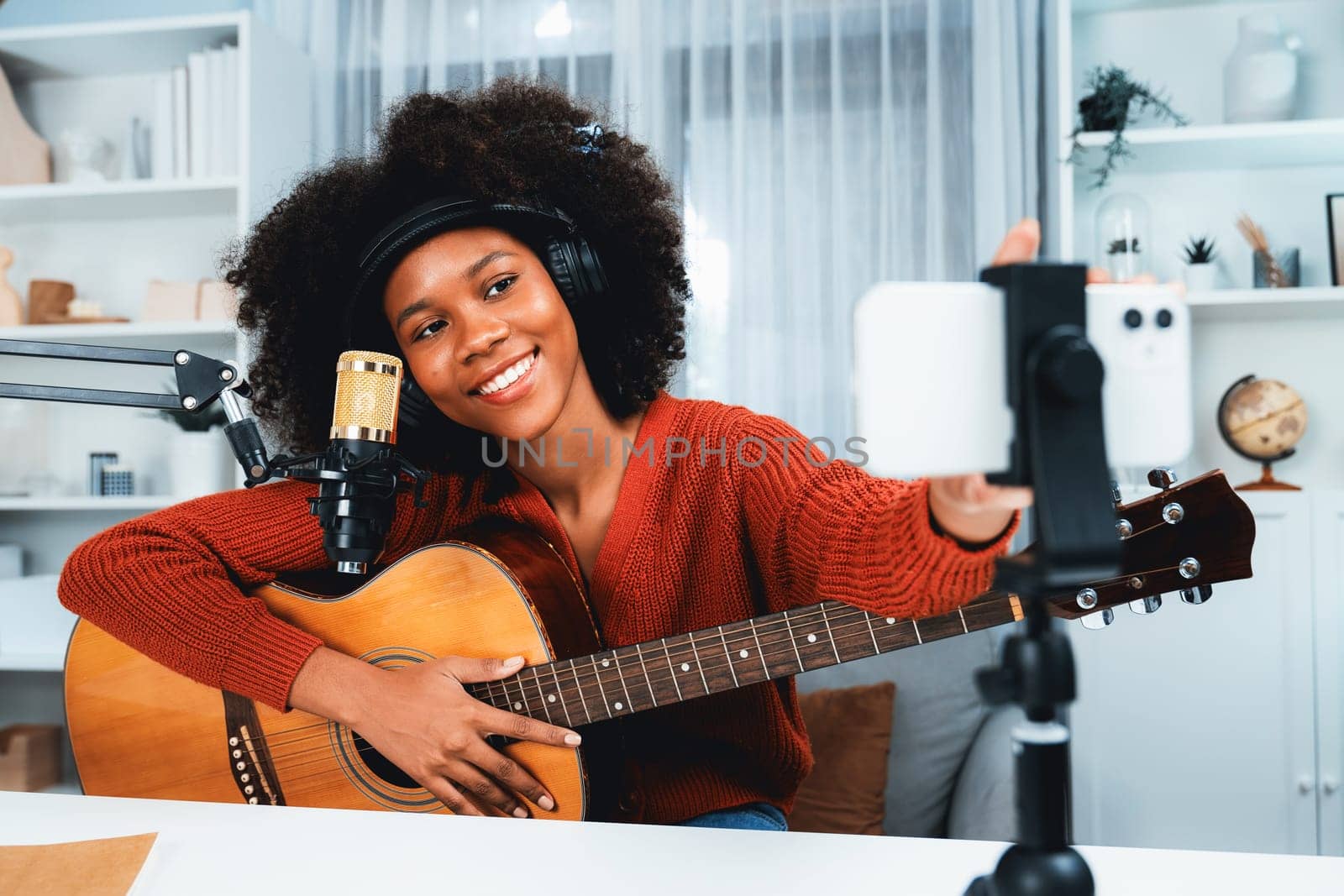 Host channel of beautiful African woman influencer setting smartphone, sing with play guitar in broadcast. Time slot of music blogger on live social media online. Concept of audio creator. Tastemaker.