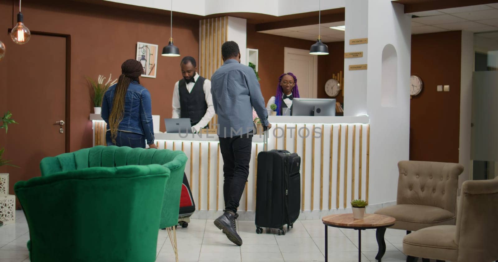 African american people arrive at hotel, talking to staff members about room booking and check in procedure. Man and woman arriving in lobby with trolley bags, honeymoon trip.