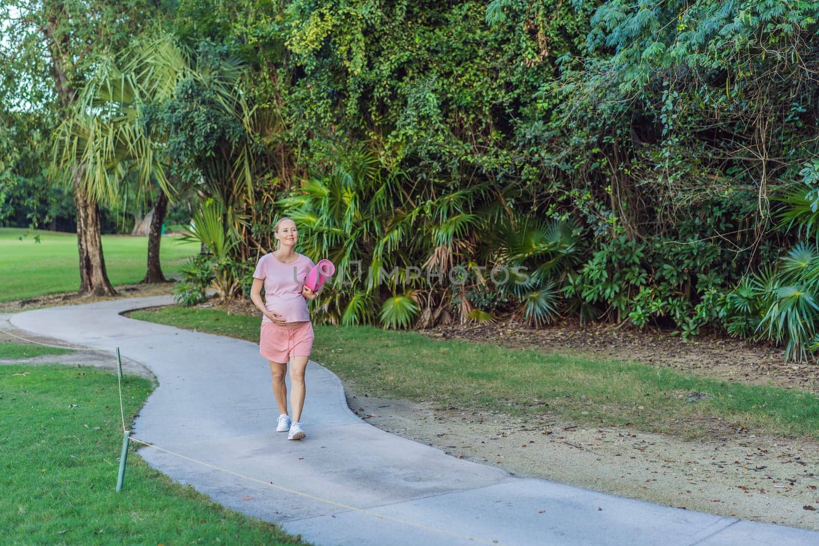 Energetic pregnant woman takes her workout outdoors, using an exercise mat for a refreshing and health-conscious outdoor exercise session.