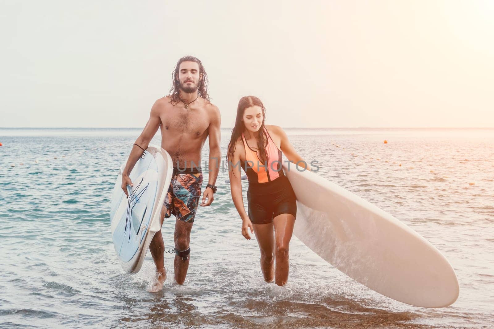 Sea woman and man on sup. Silhouette of happy young woman and man, surfing on SUP board, confident paddling through water surface. Idyllic sunset. Active lifestyle at sea or river