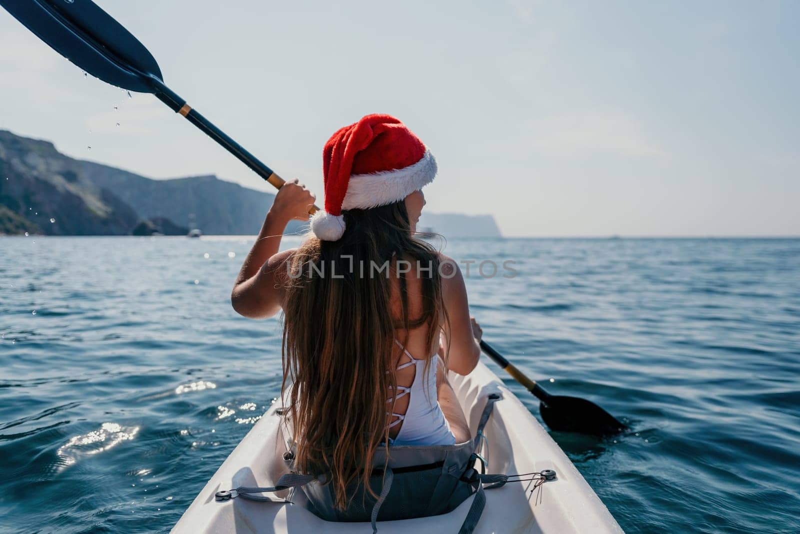 Woman in kayak back view. Happy young woman with long hair floating in transparent kayak on the crystal clear sea. Summer holiday vacation and cheerful female people relaxing having fun on the boat