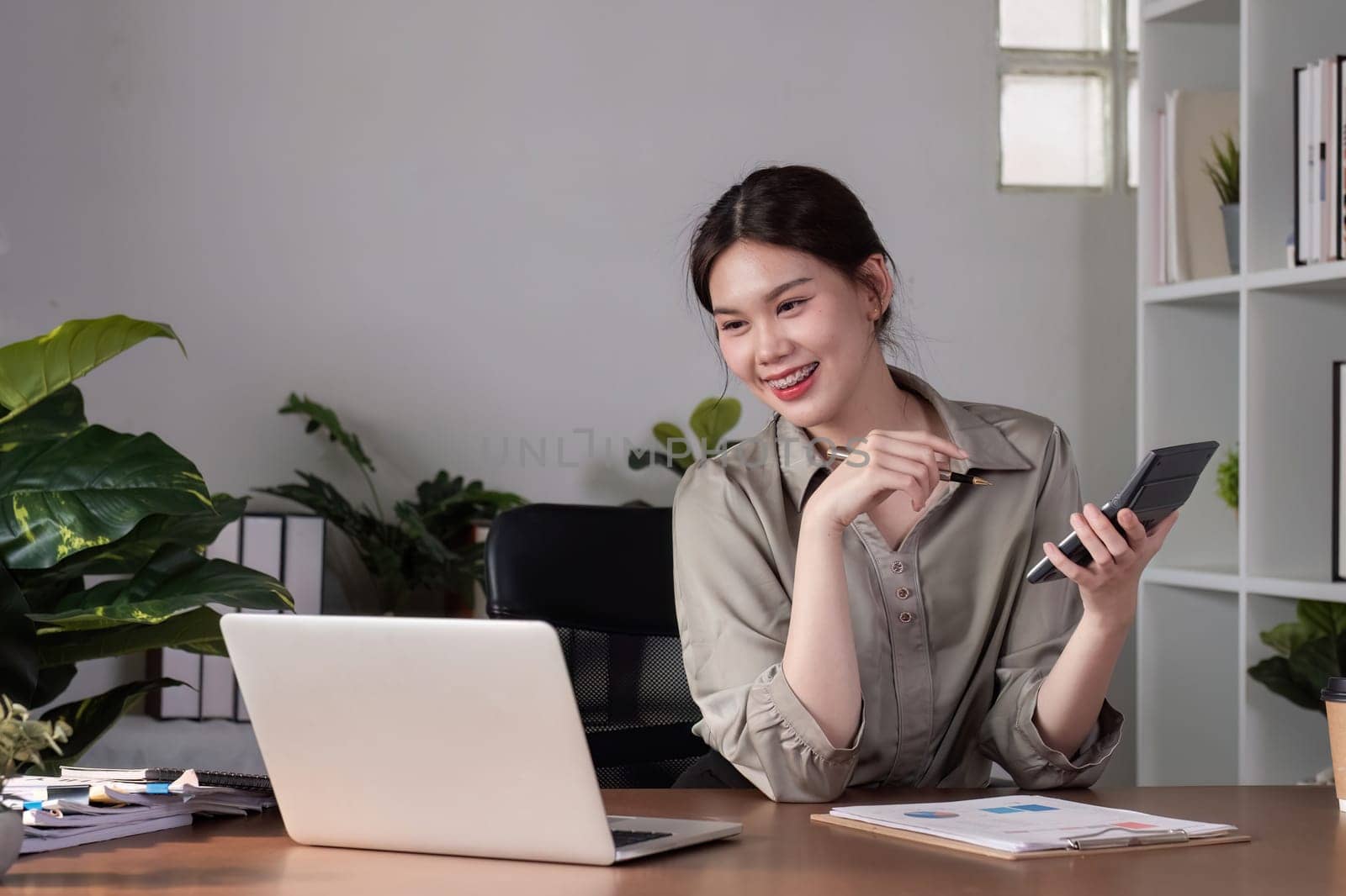 Young Asian business woman sitting in the office using a calculator to calculate business numbers..