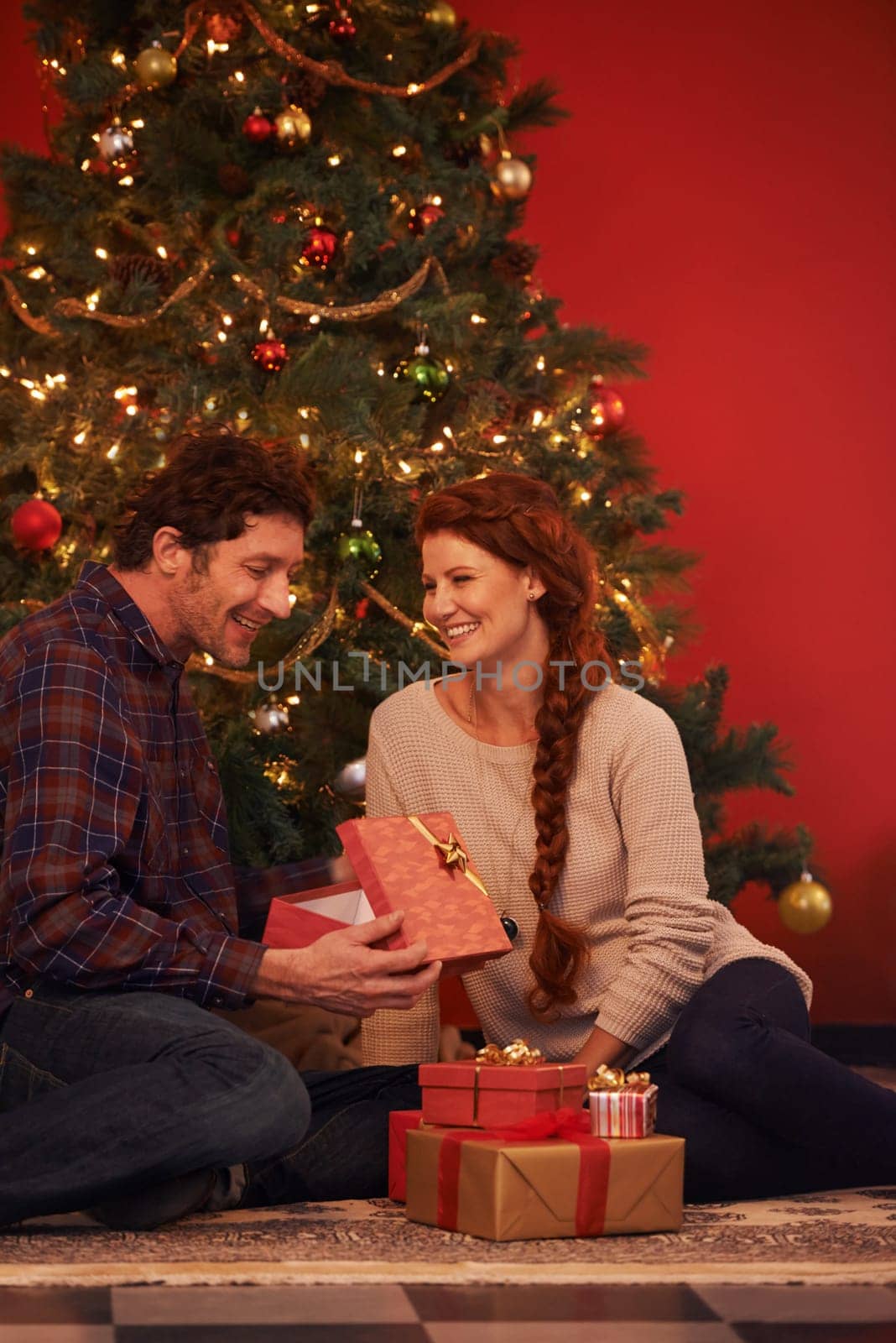 Couple, tree for Christmas and gift for holiday celebration, festive season of giving for love and commitment. Happy, gratitude and support with people at home for present, romance and relationship.