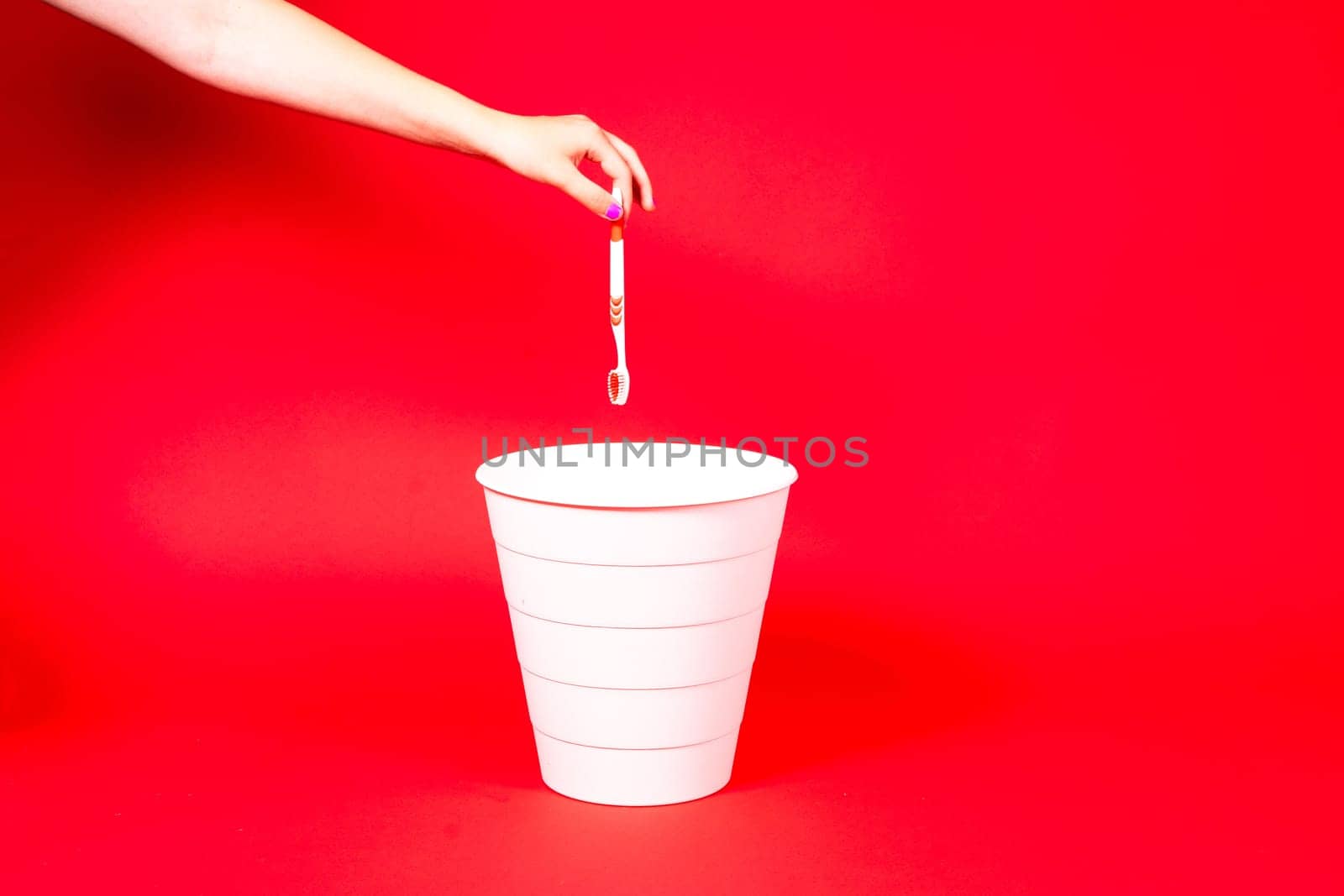 The toothbrush is thrown into a trash basket. Red background, copy space.