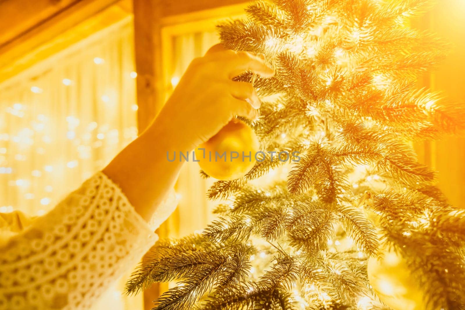 Woman decorate A Christmas tree with gold ornaments and lights. The tree is decorated with gold balls and is lit up with lights. by panophotograph