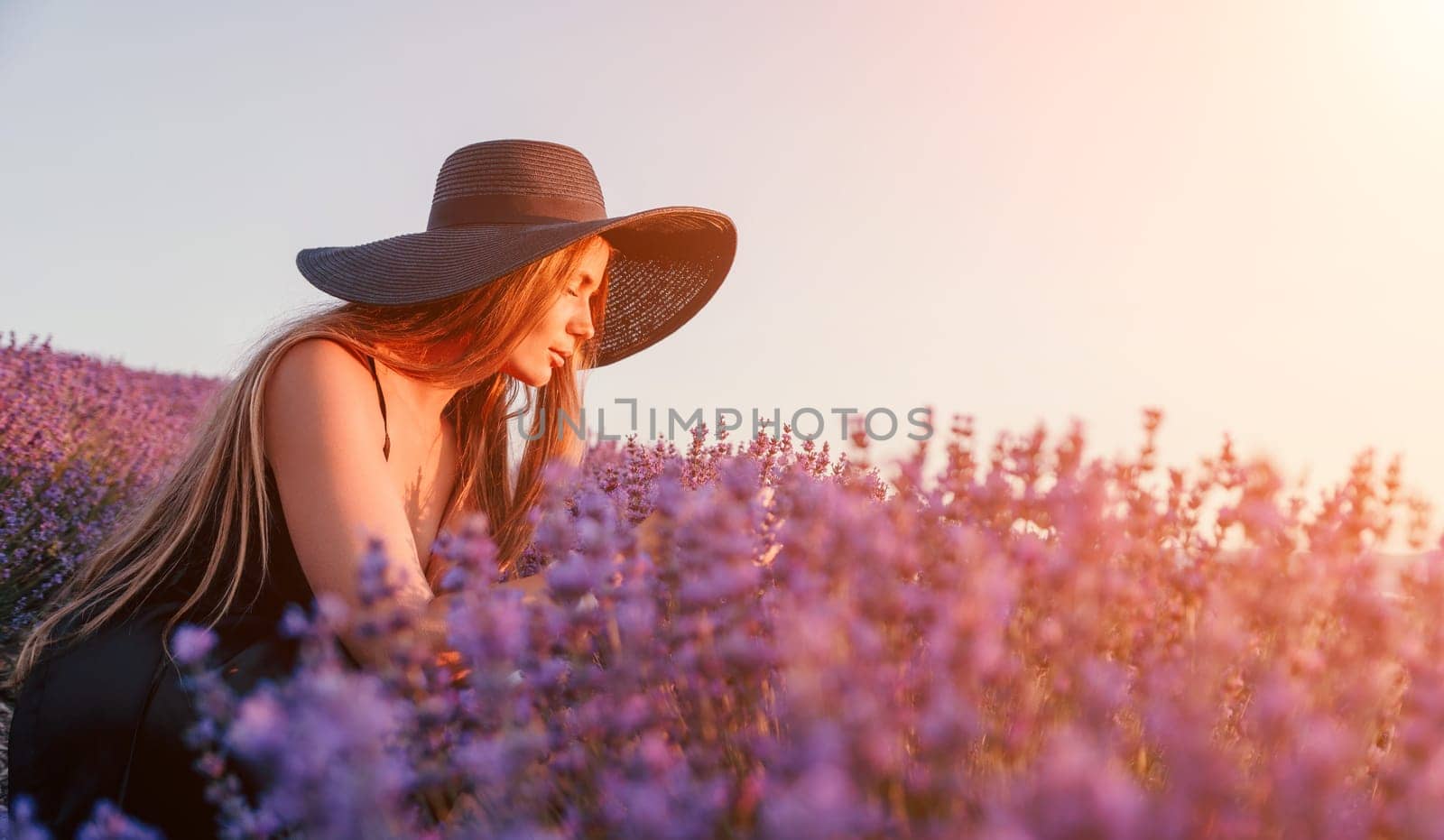 Close up portrait of young beautiful woman in a white dress and a hat is walking in the lavender field and smelling lavender bouquet.