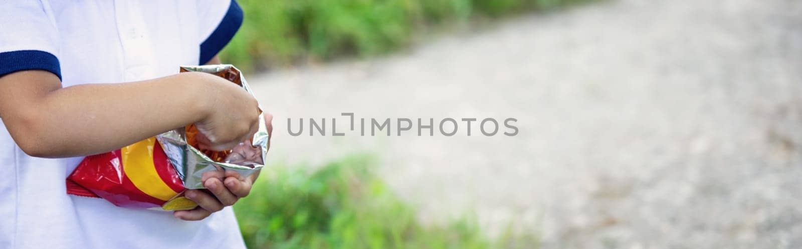 a child eats chips from a pack on the background of nature