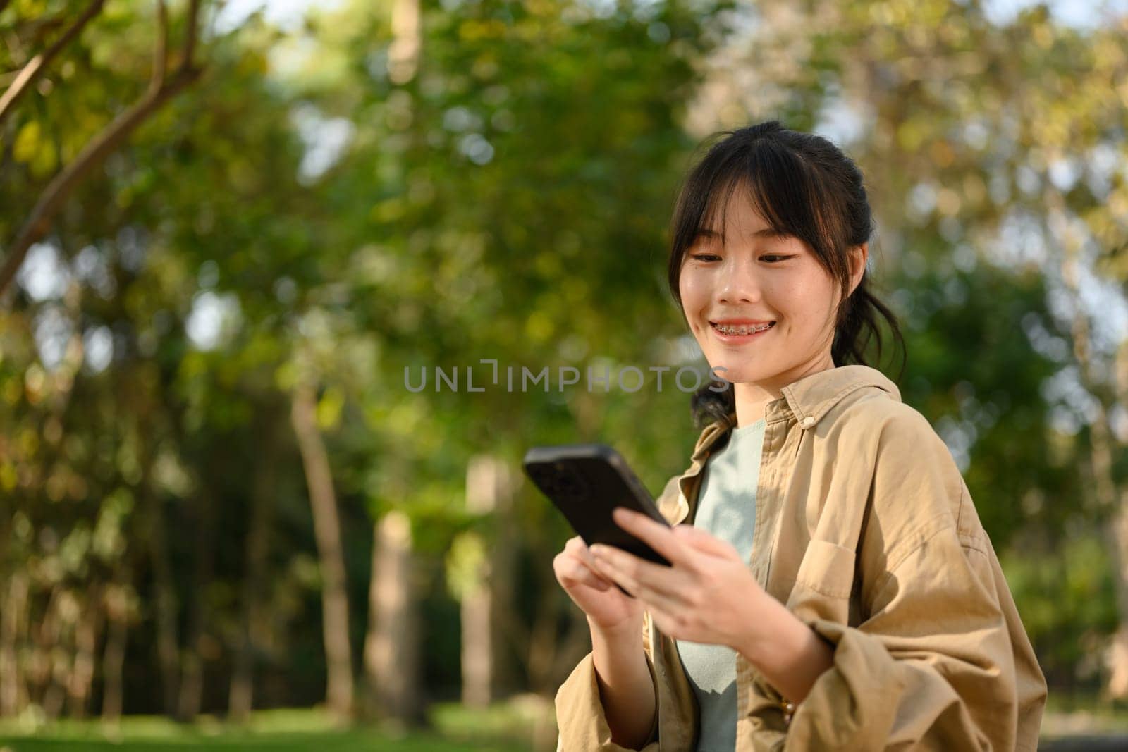 Attractive young woman sitting on bench in park and texting on her mobile phone by prathanchorruangsak