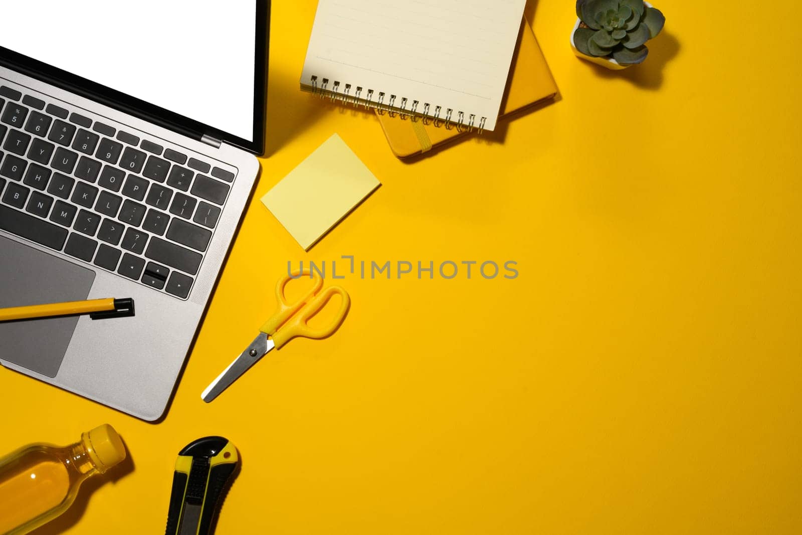 Top view of laptop with empty display, water bottle and office supplies on yellow background.