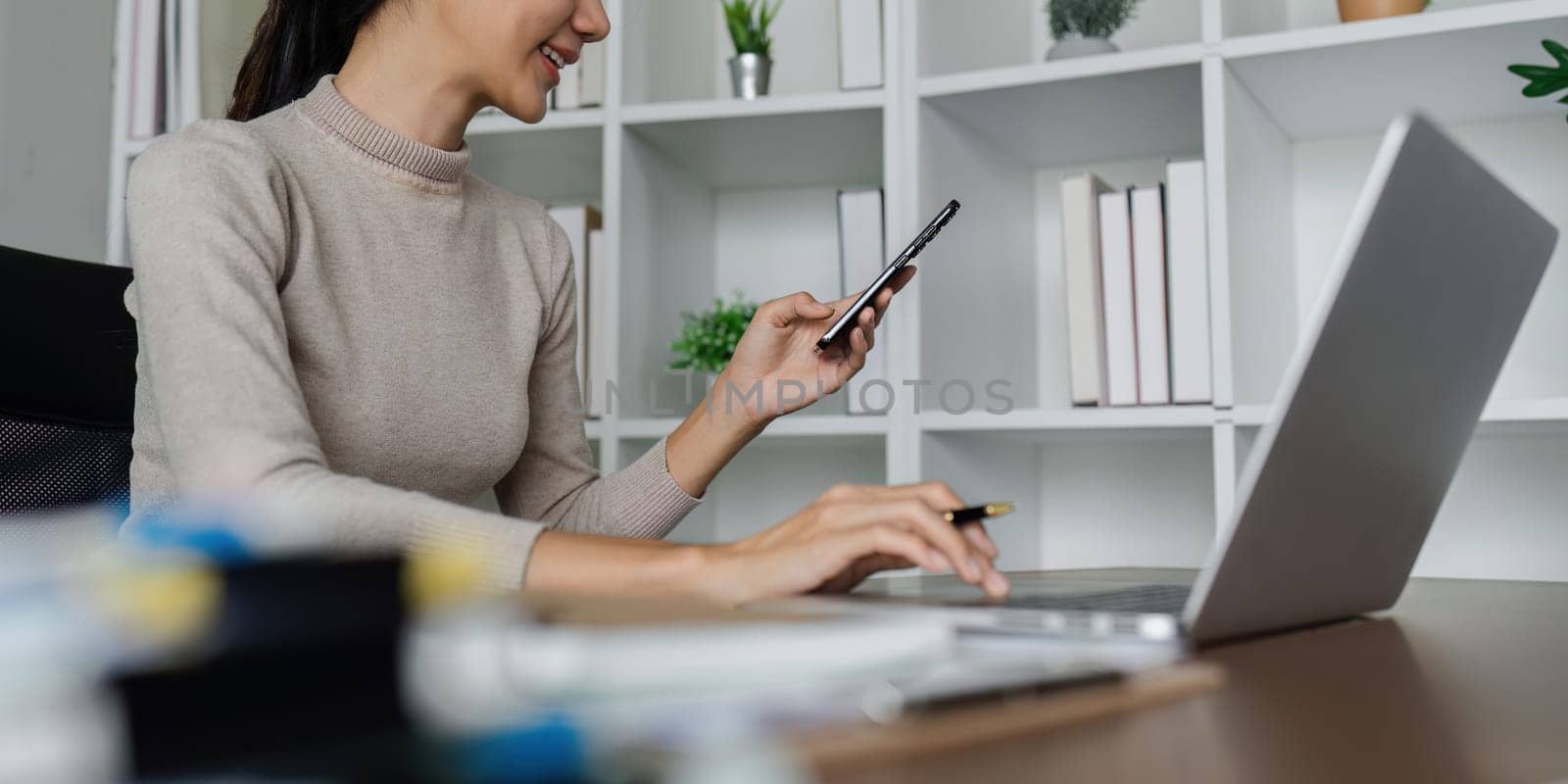 business woman using smartphone while working on laptop, synchronize data between computer and gadget at home, use corporate devices and business application by itchaznong