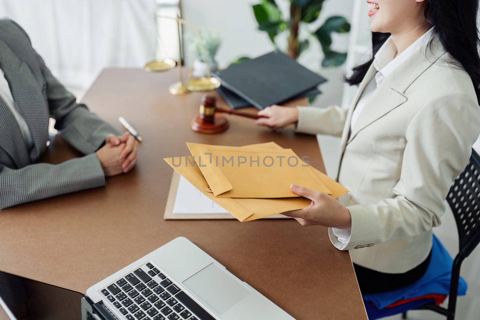 A woman is sitting at a desk with a stack of envelopes in front of her. She is holding the envelopes and she is in a professional setting