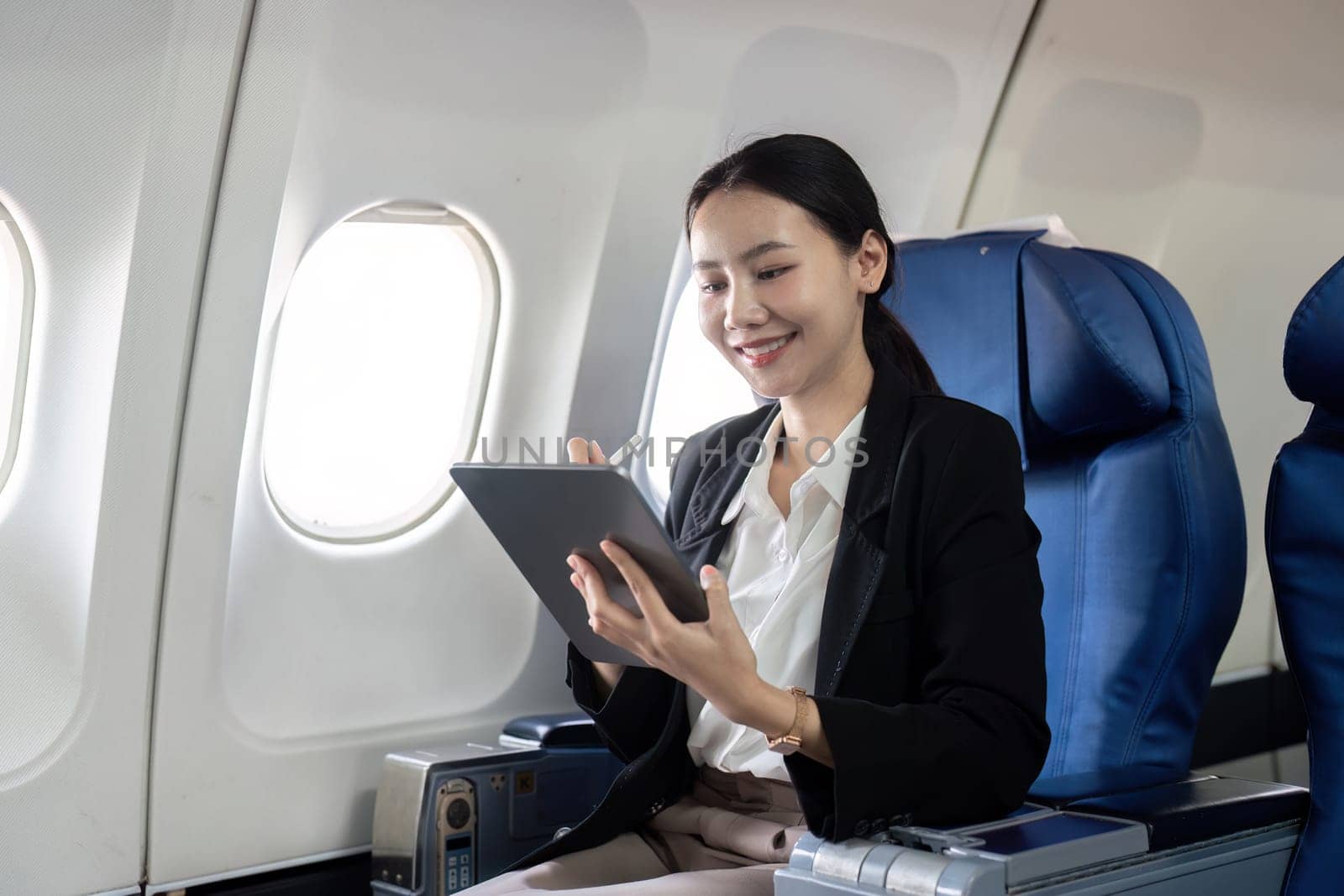 Smiling happy business woman asian flying and working in an airplane in first class, Woman sitting inside an airplane using digital tablet by nateemee
