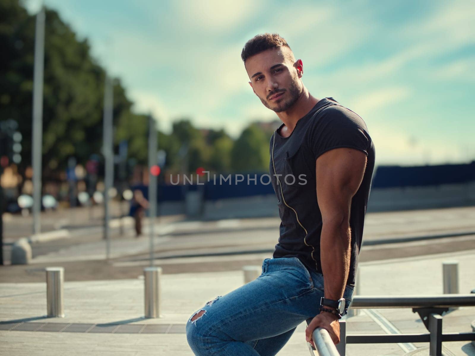 A man is seated on the metal bench, looking out into the distance. He appears relaxed and thoughtful as he takes in the surroundings.