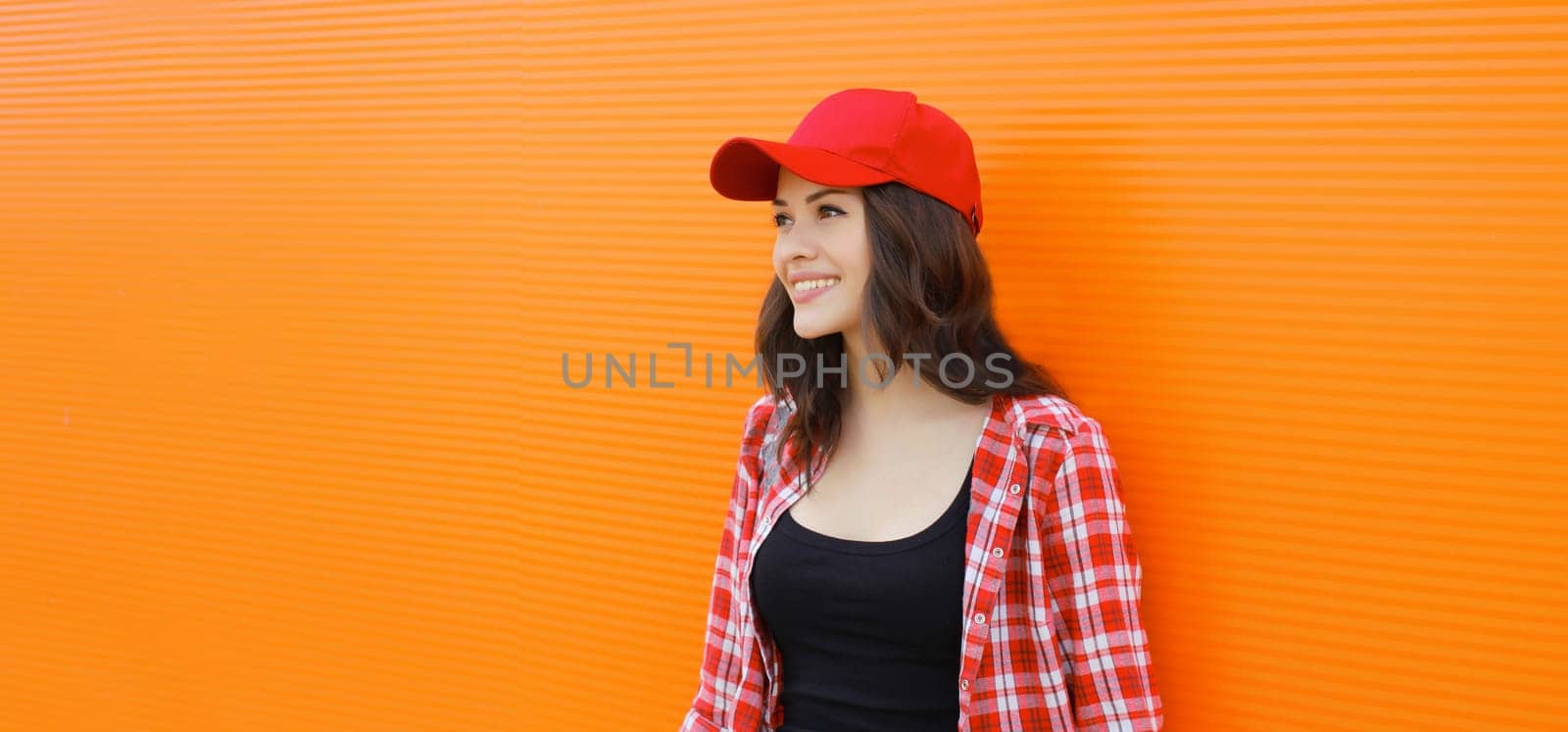 Summer portrait of happy smiling young woman posing in red baseball cap, casual clothes on city street