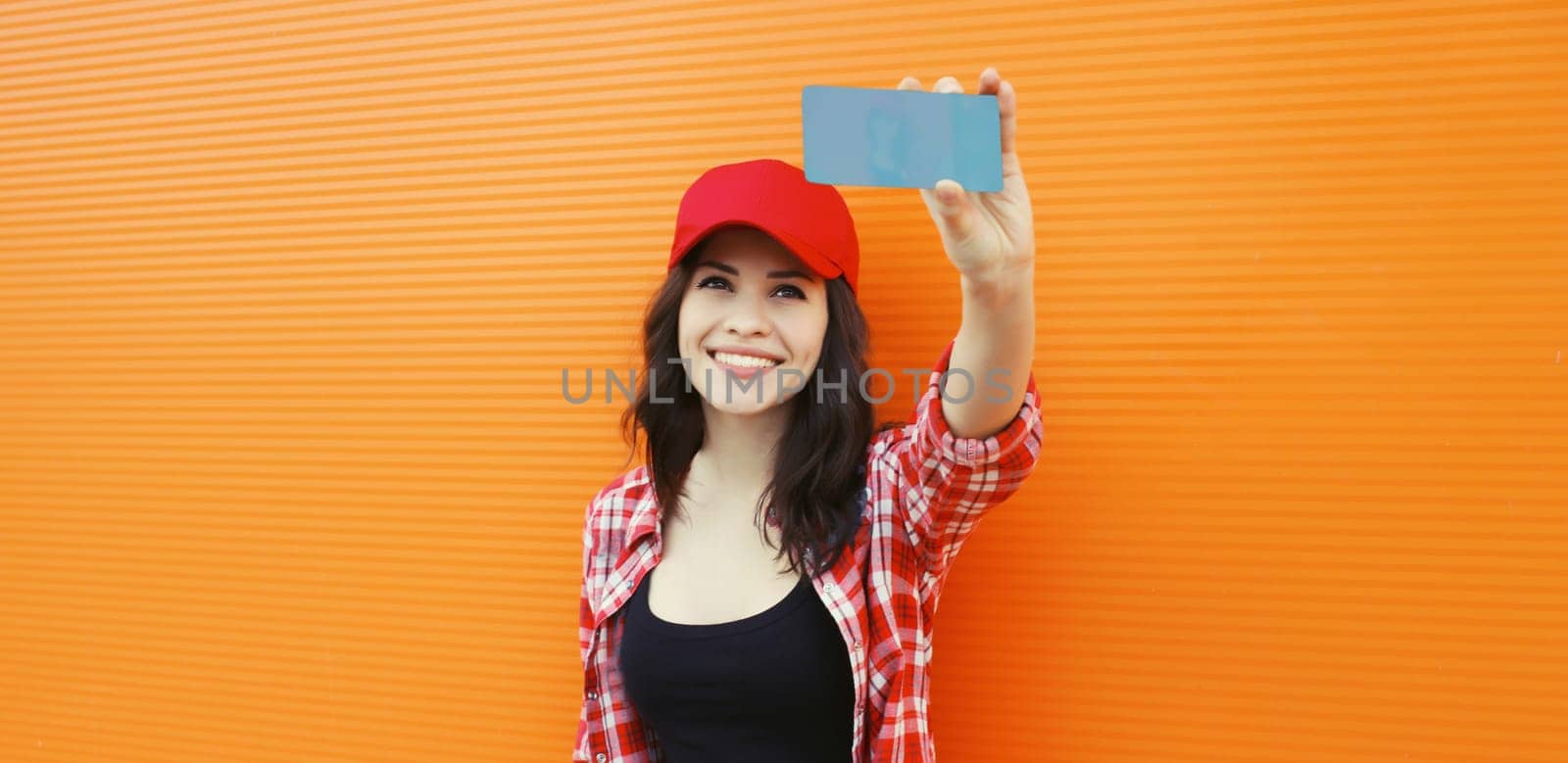 Happy cheerful smiling young woman taking selfie with mobile phone on colorful orange background by Rohappy