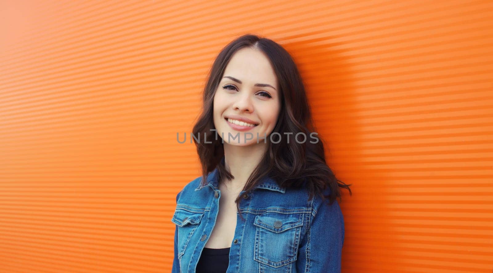 Portrait of happy smiling brunette young woman looking at camera posing on orange background