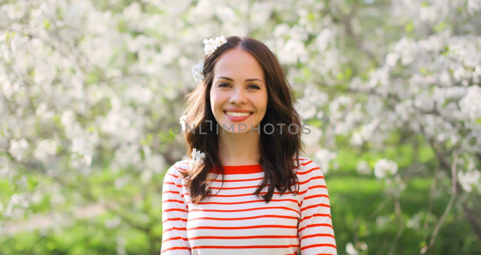 Portrait of lovely happy smiling young woman in spring blooming garden with white flowers on the trees in park