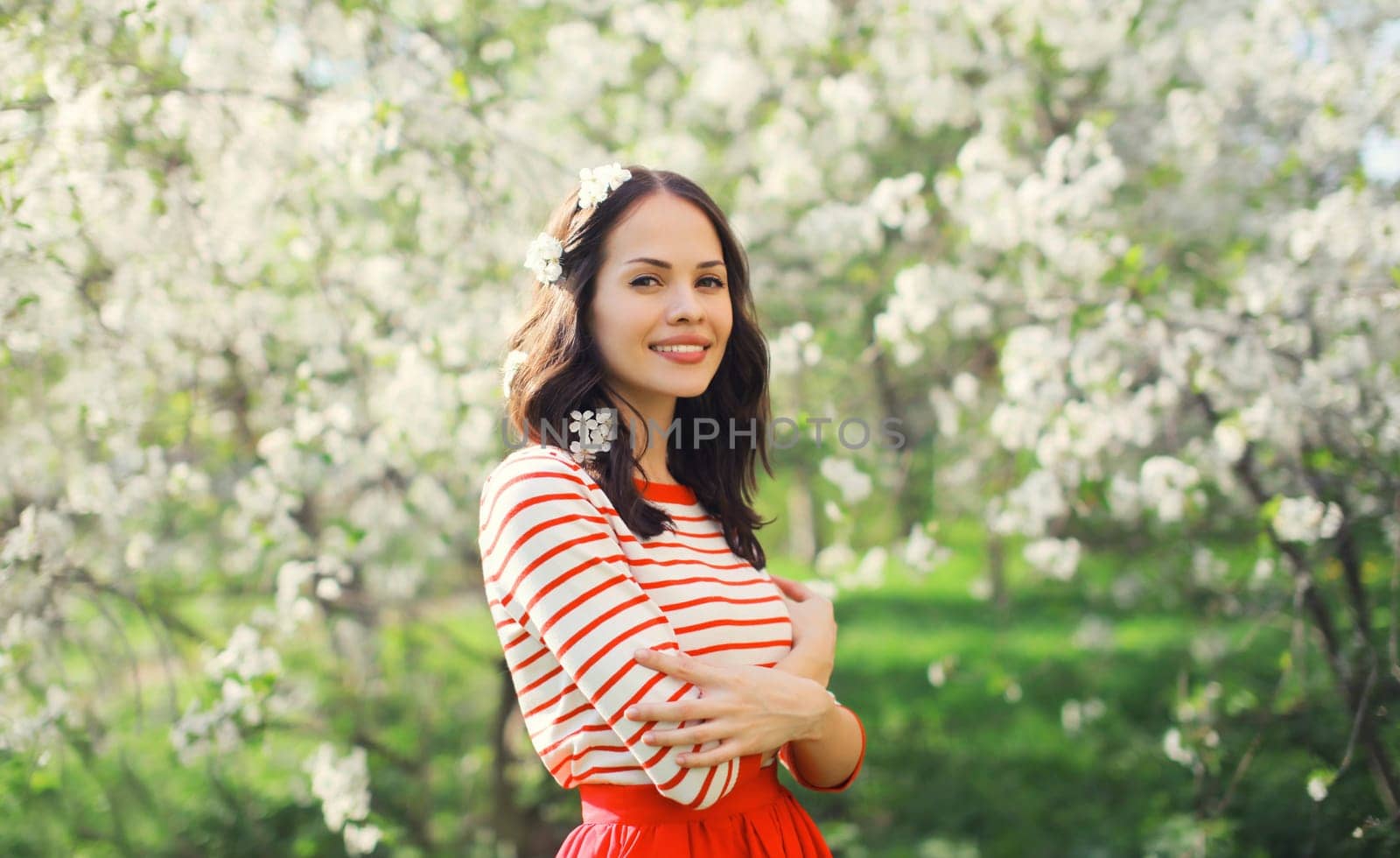 Portrait of lovely happy smiling young woman in spring blooming garden with white flowers on the trees in park