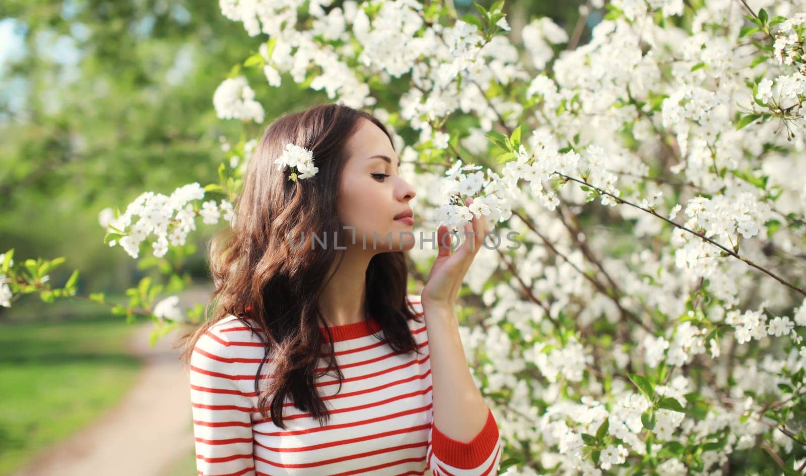 Portrait of lovely happy smiling young woman in spring blooming garden with white flowers on the trees in park