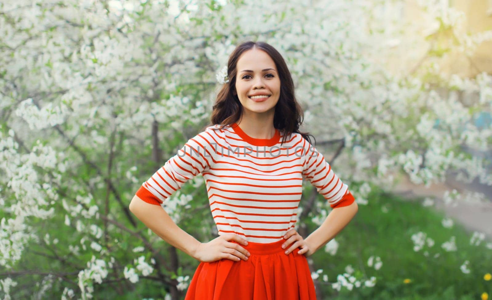 Portrait of lovely happy smiling young woman in spring blooming garden with white flowers on the trees in park