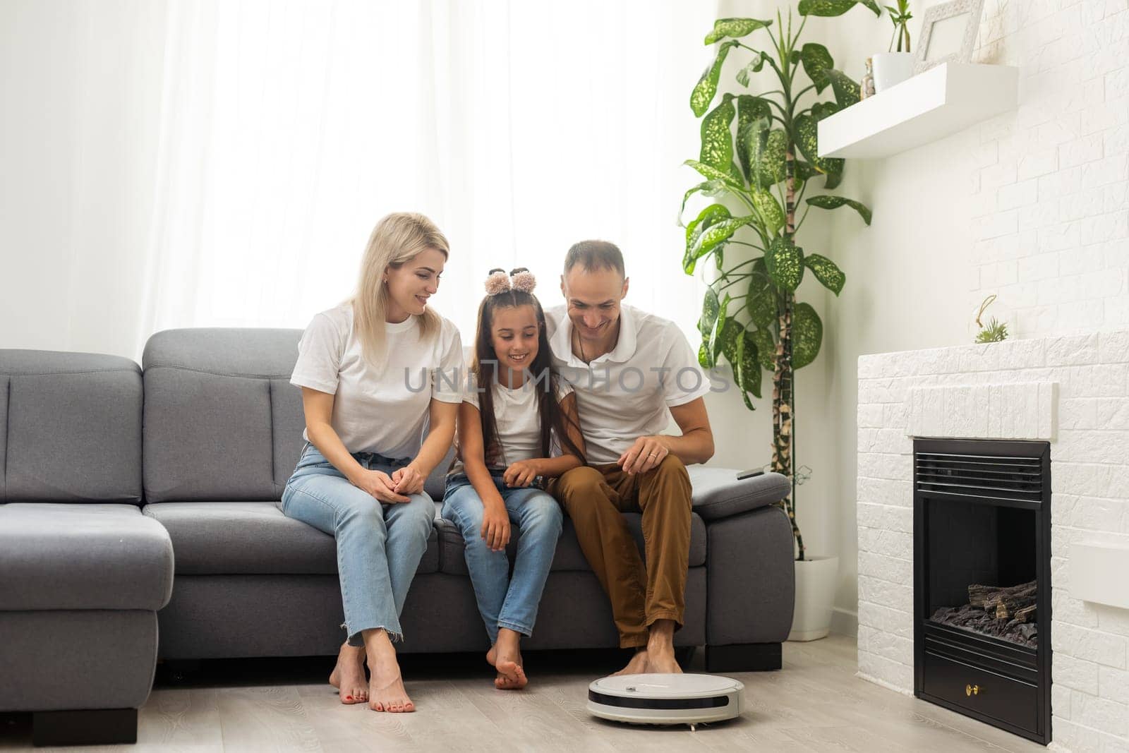 Family resting while robotic vacuum cleaner doing its work at home.