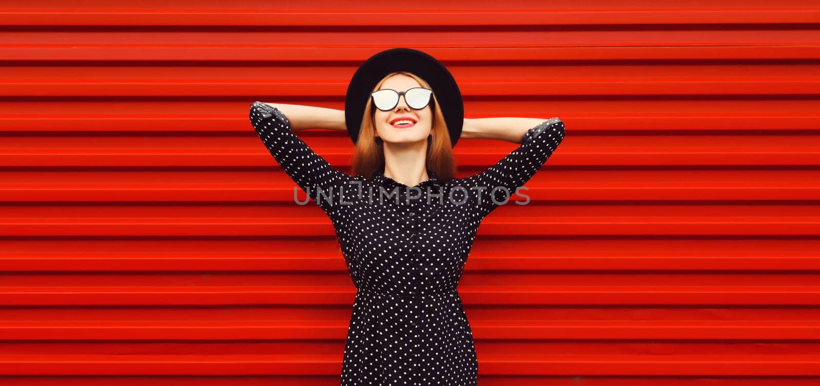 Portrait of beautiful smiling young woman wearing black round hat on red background
