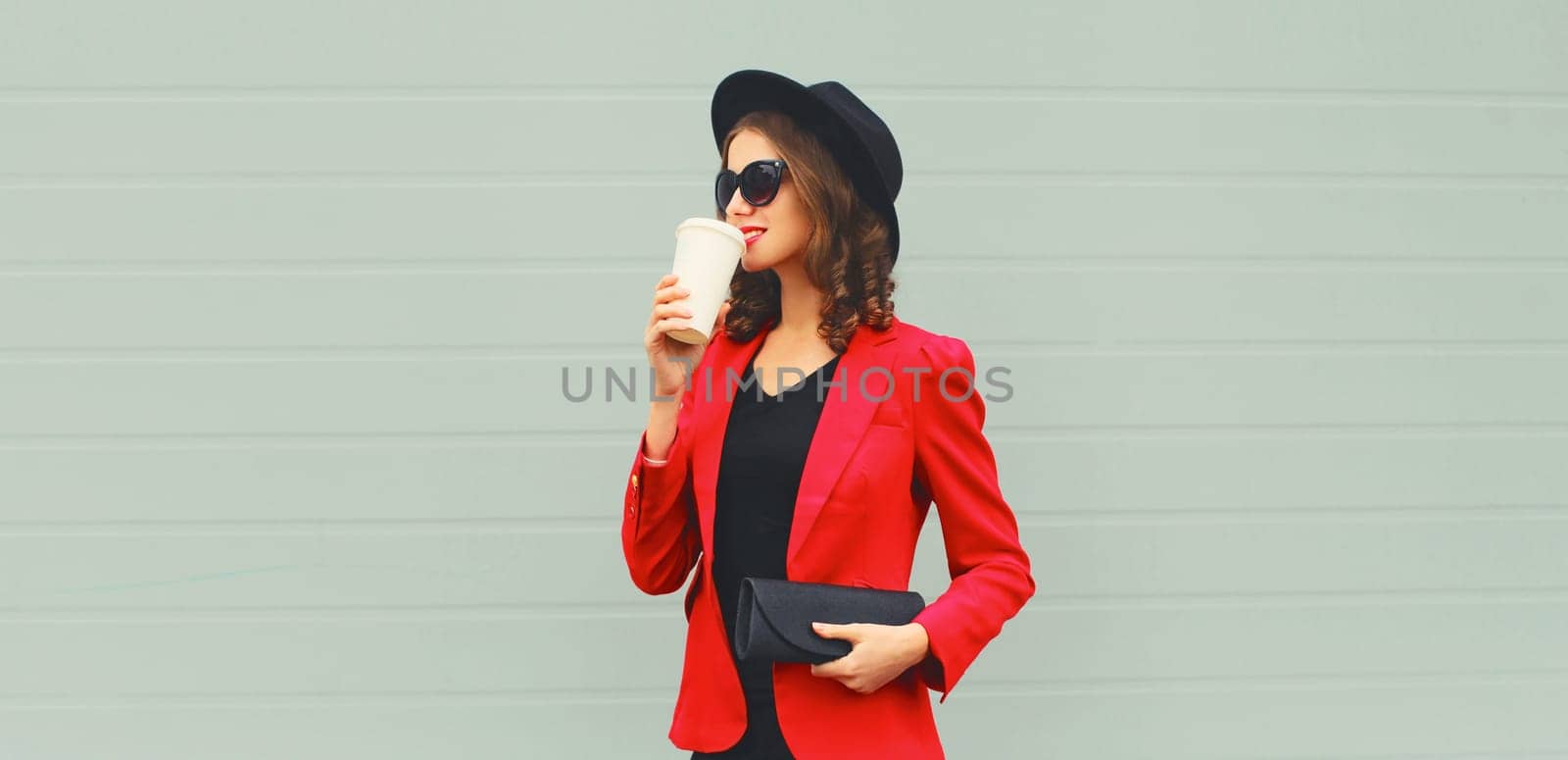 Stylish elegant woman posing in business suit, red blazer jacket, black round hat with handbag clutch