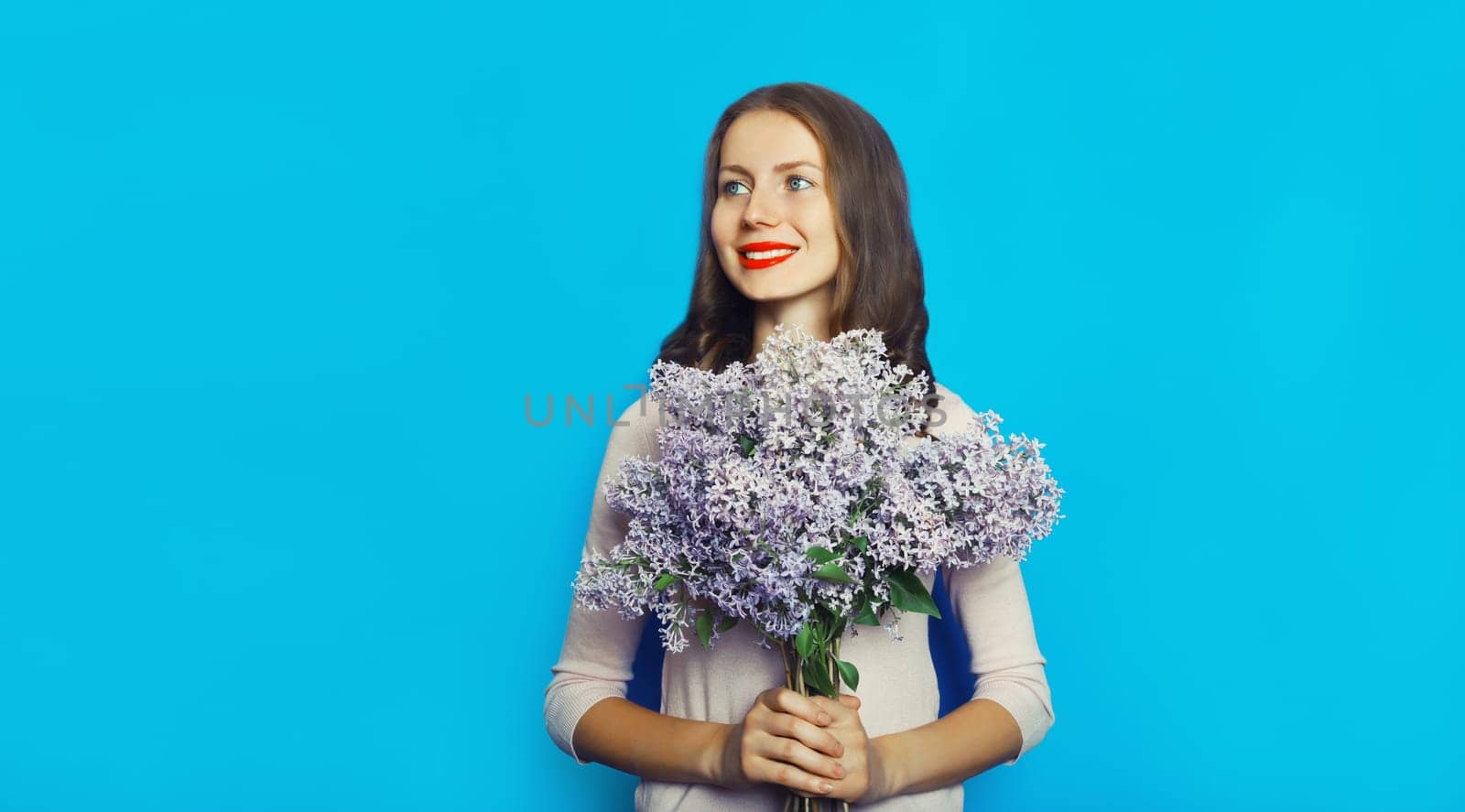 Portrait of beautiful happy smiling woman with bouquet of fresh lilac flowers, wildflowers on blue background