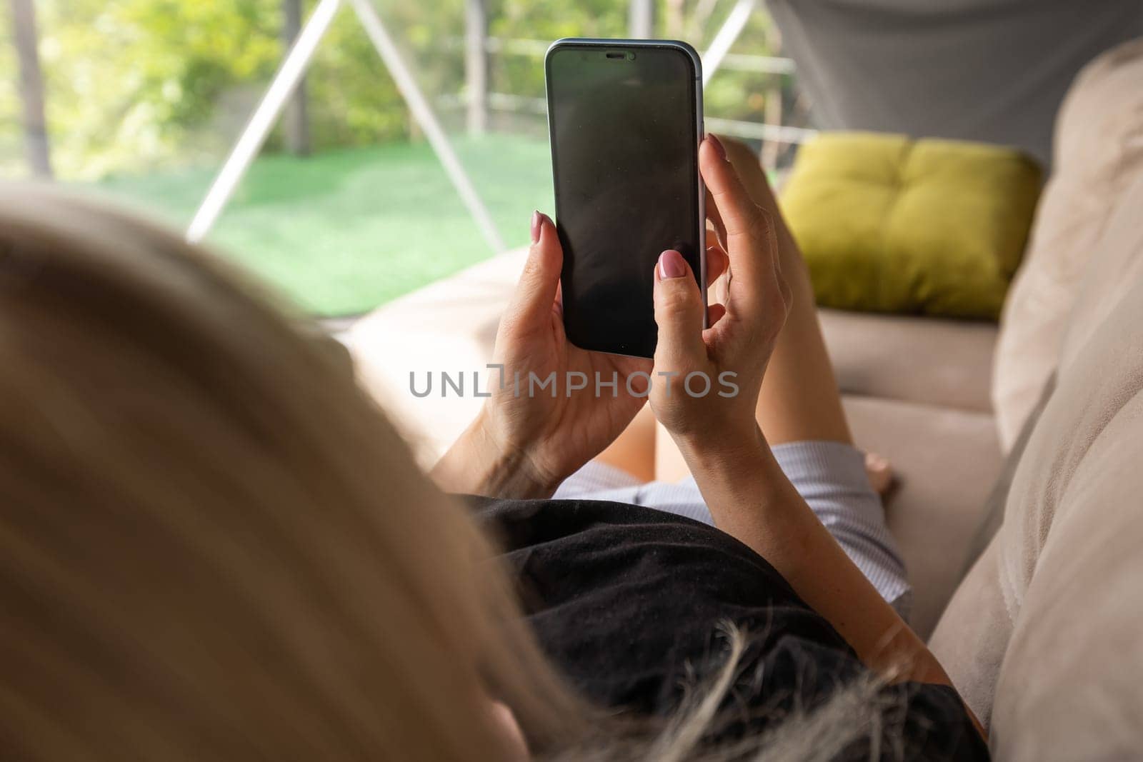 Happy young caucasian woman relax on comfortable couch at home texting messaging on smartphone, use cellphone, browse wireless internet on gadget, shopping online from home by Andelov13