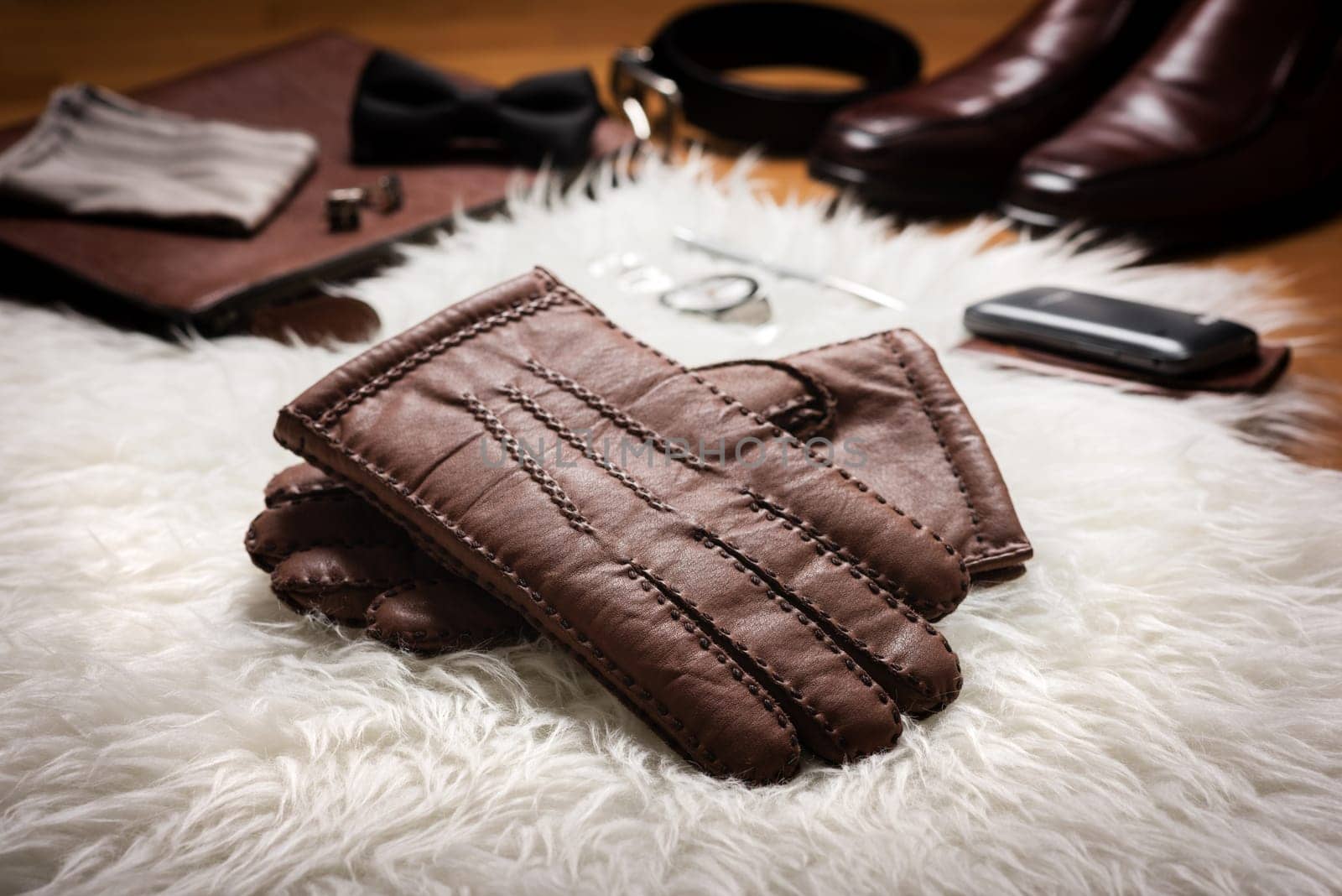 Pair of men's brown leather gloves and other men's accessories over white fur.