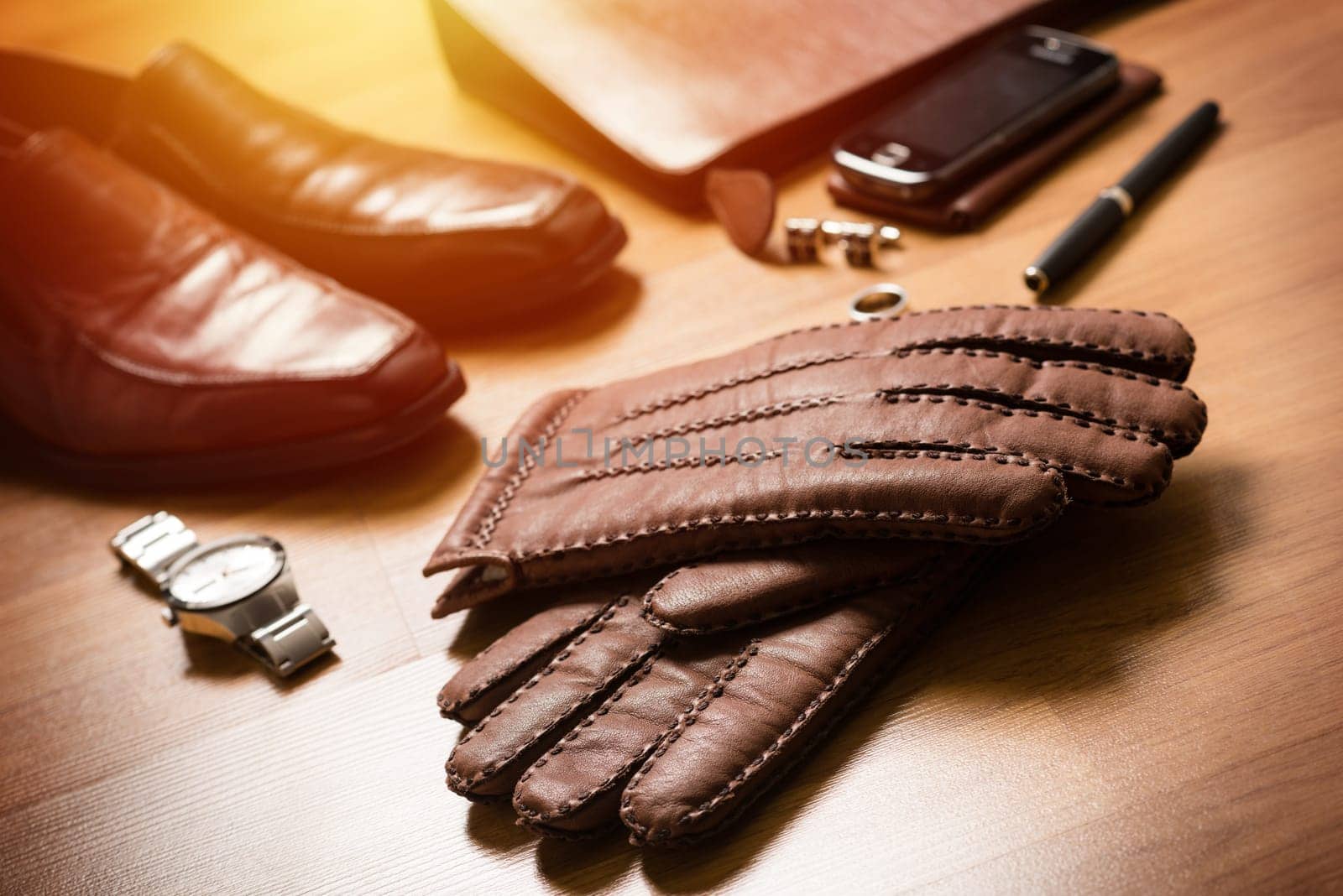 Pair of men's brown leather gloves and other men's accessories on the floor.