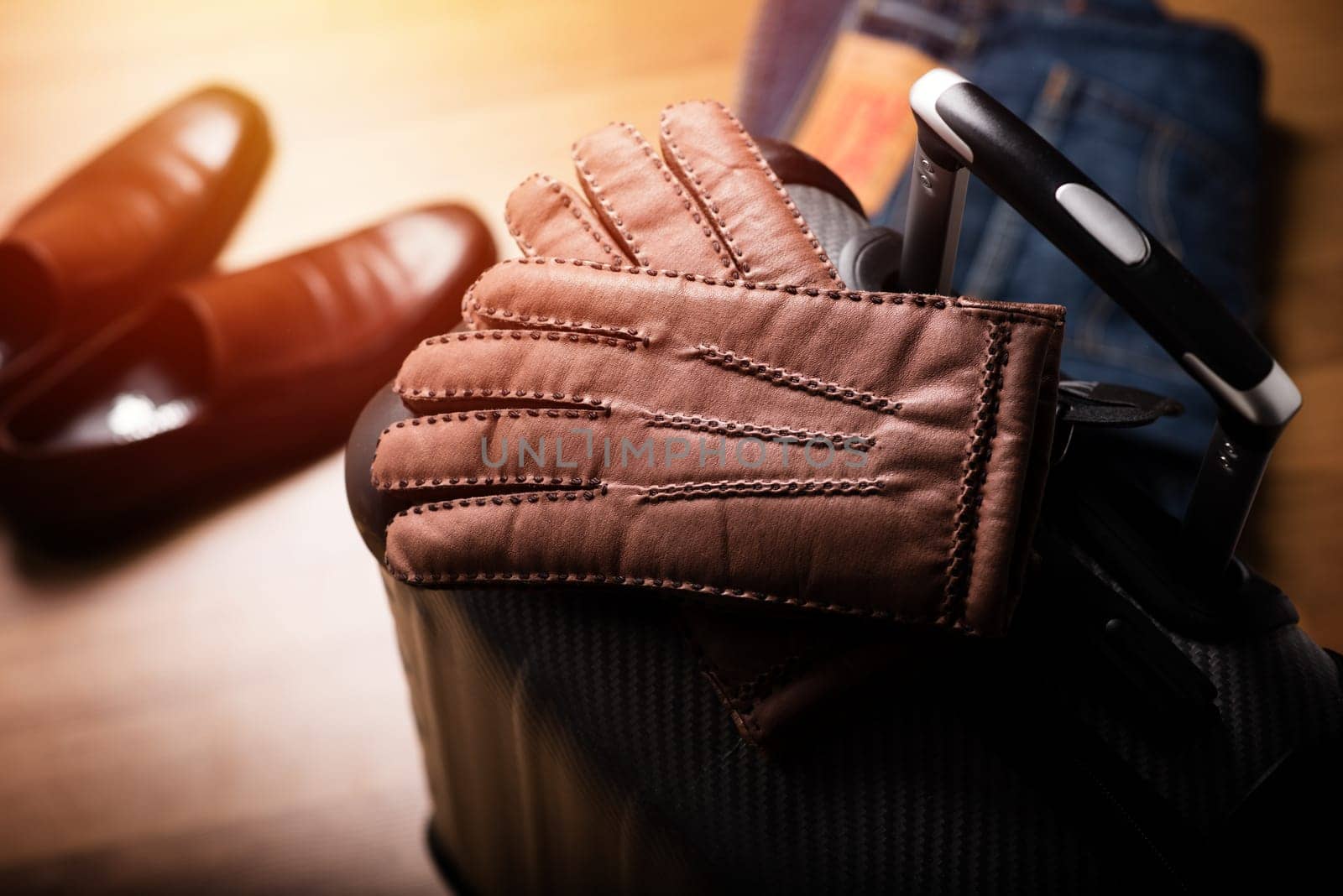 Pair of men's brown leather gloves and other men's accessories on the luggage.