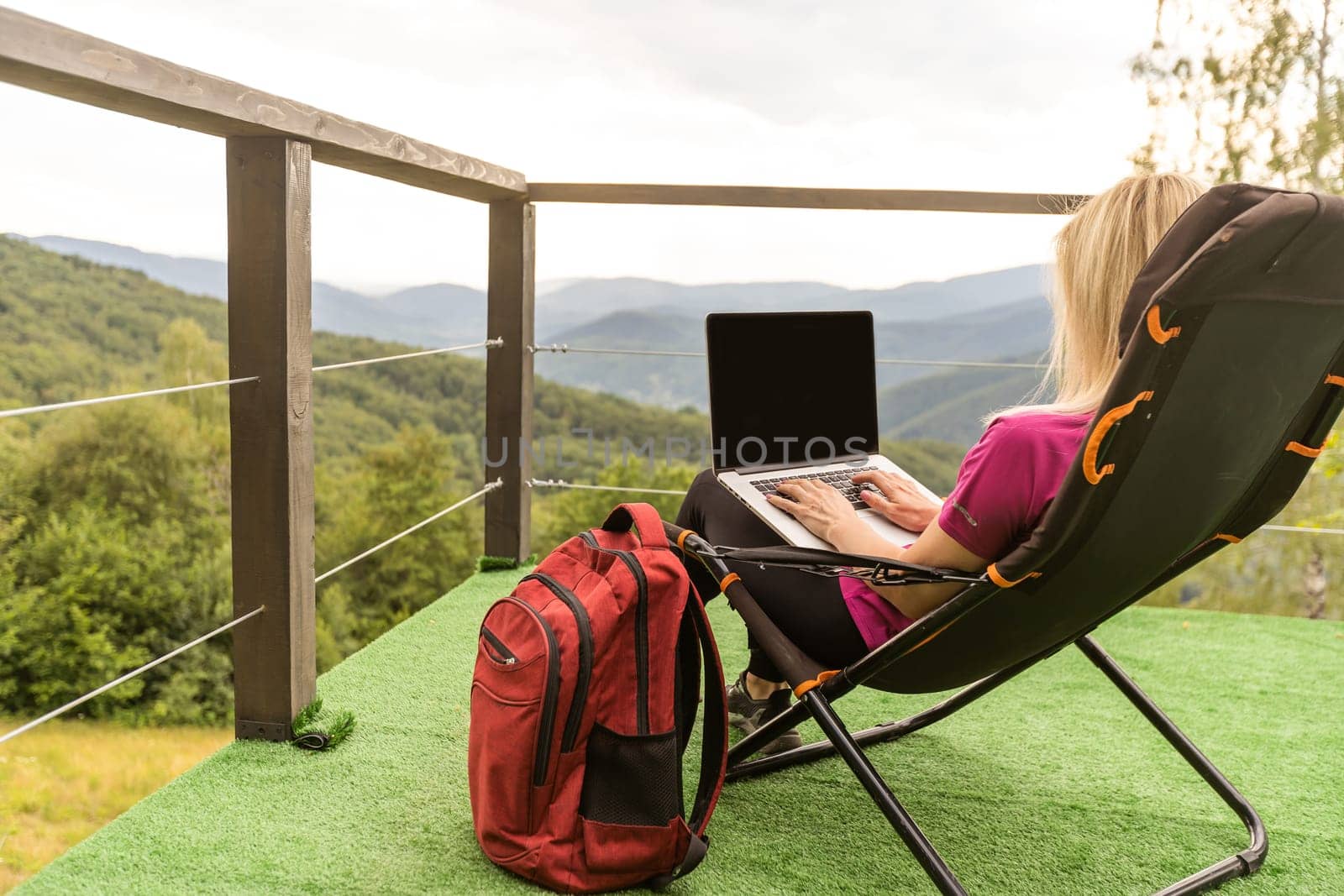 A woman in a sports warm suit works on a laptop outdoors in a mountainous area
