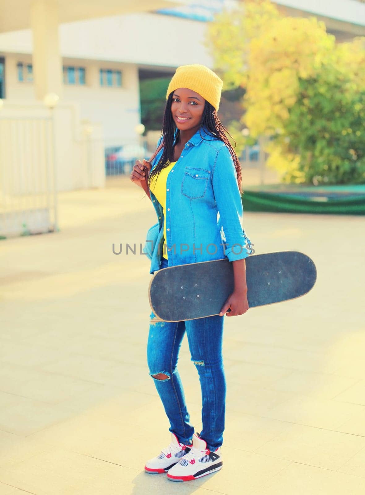 Portrait of happy smiling young african woman with skateboard in the city