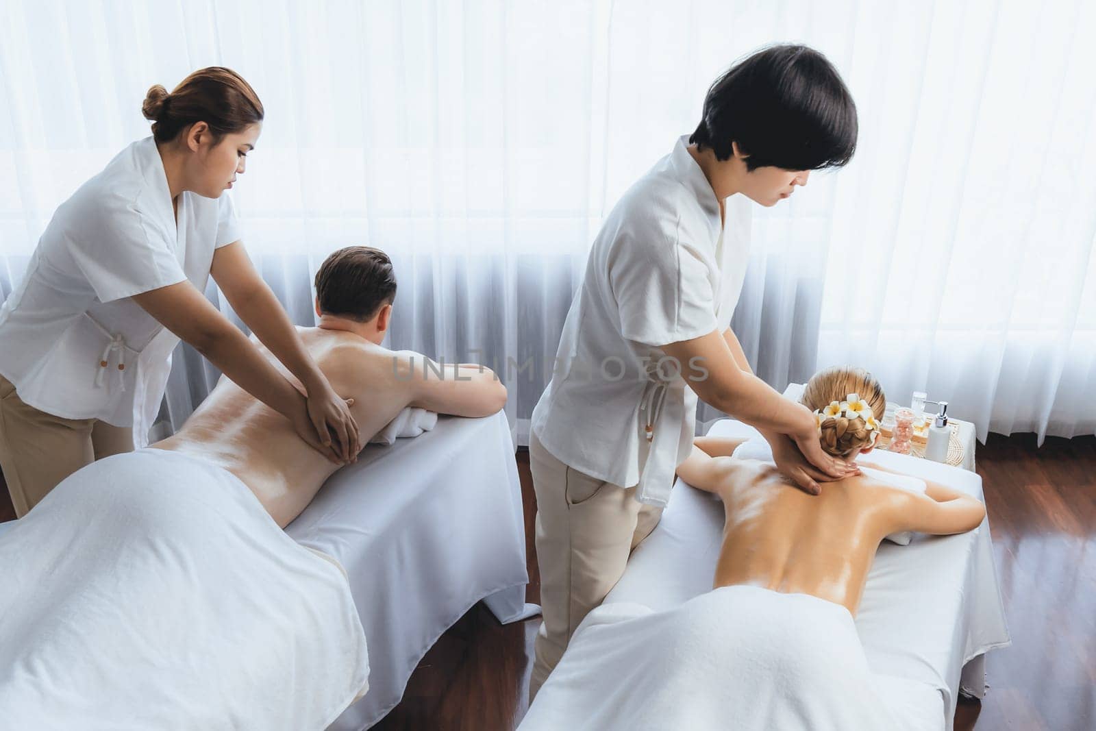 Caucasian couple customer enjoying relaxing anti-stress spa massage and pampering with beauty skin recreation leisure in day light ambient salon spa at luxury resort or hotel. Quiescent